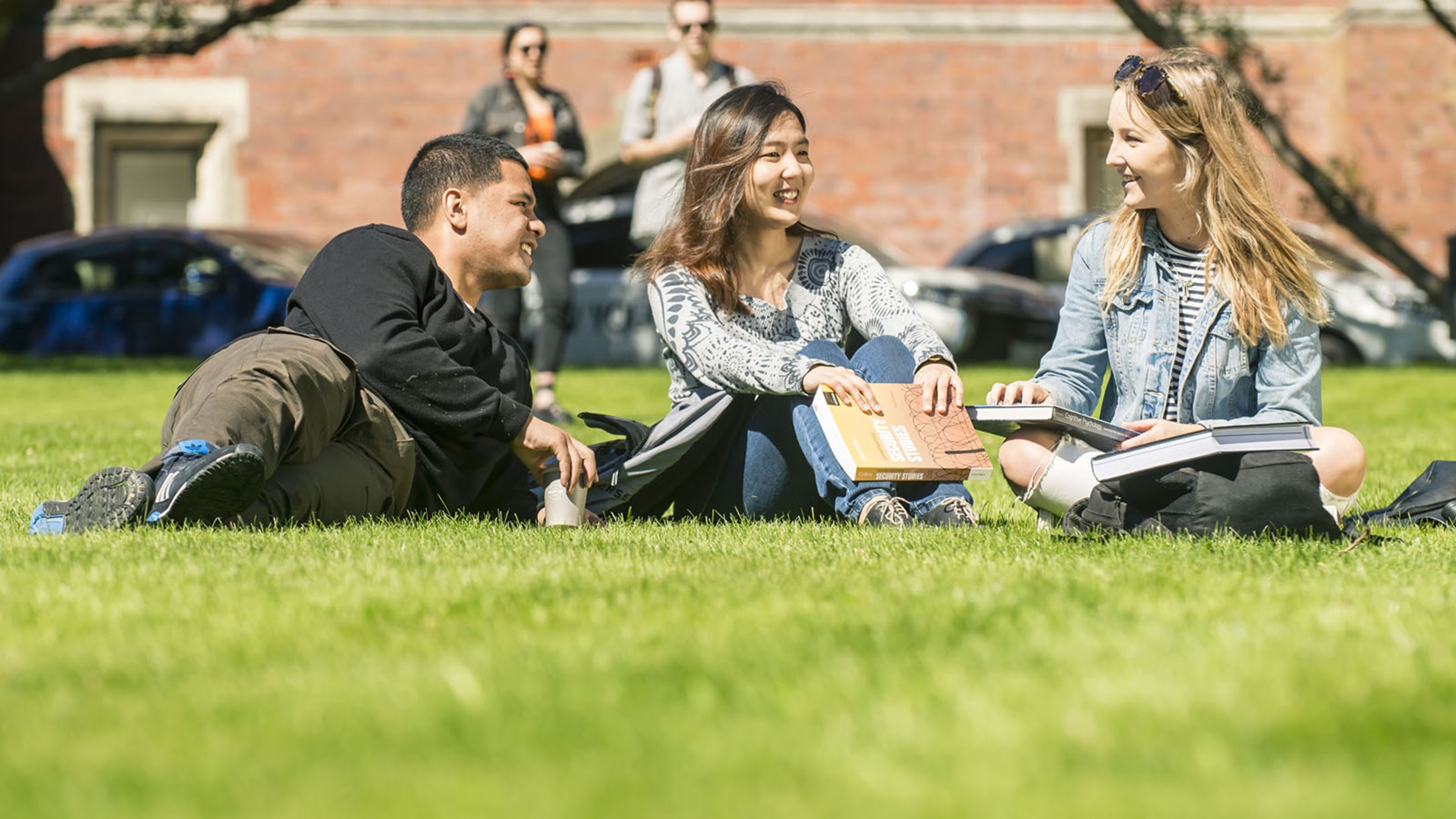 Three students lie in the sun on a lawn