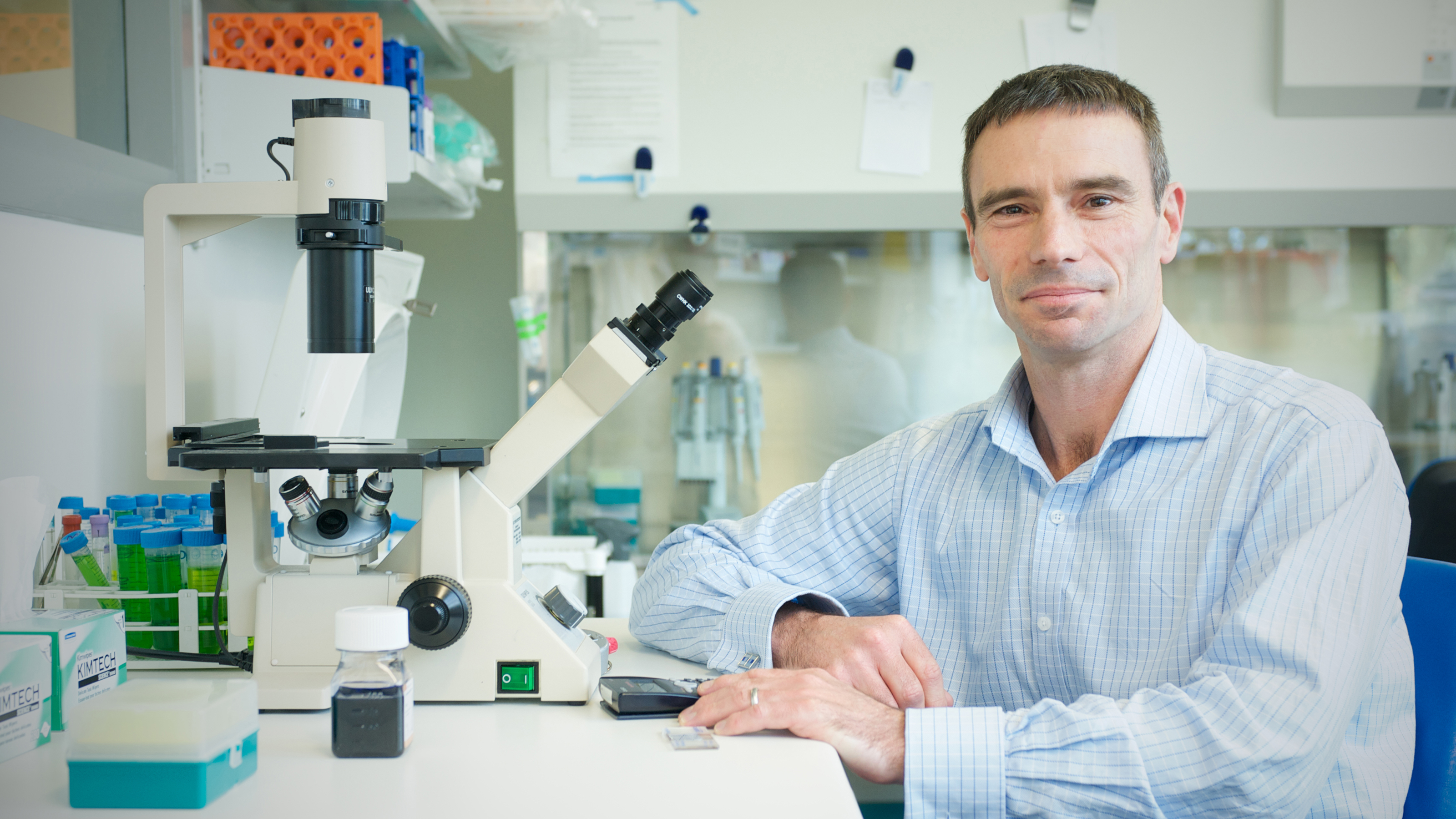 Photograph of Gavin Painter sitting with a microscope in a lab.