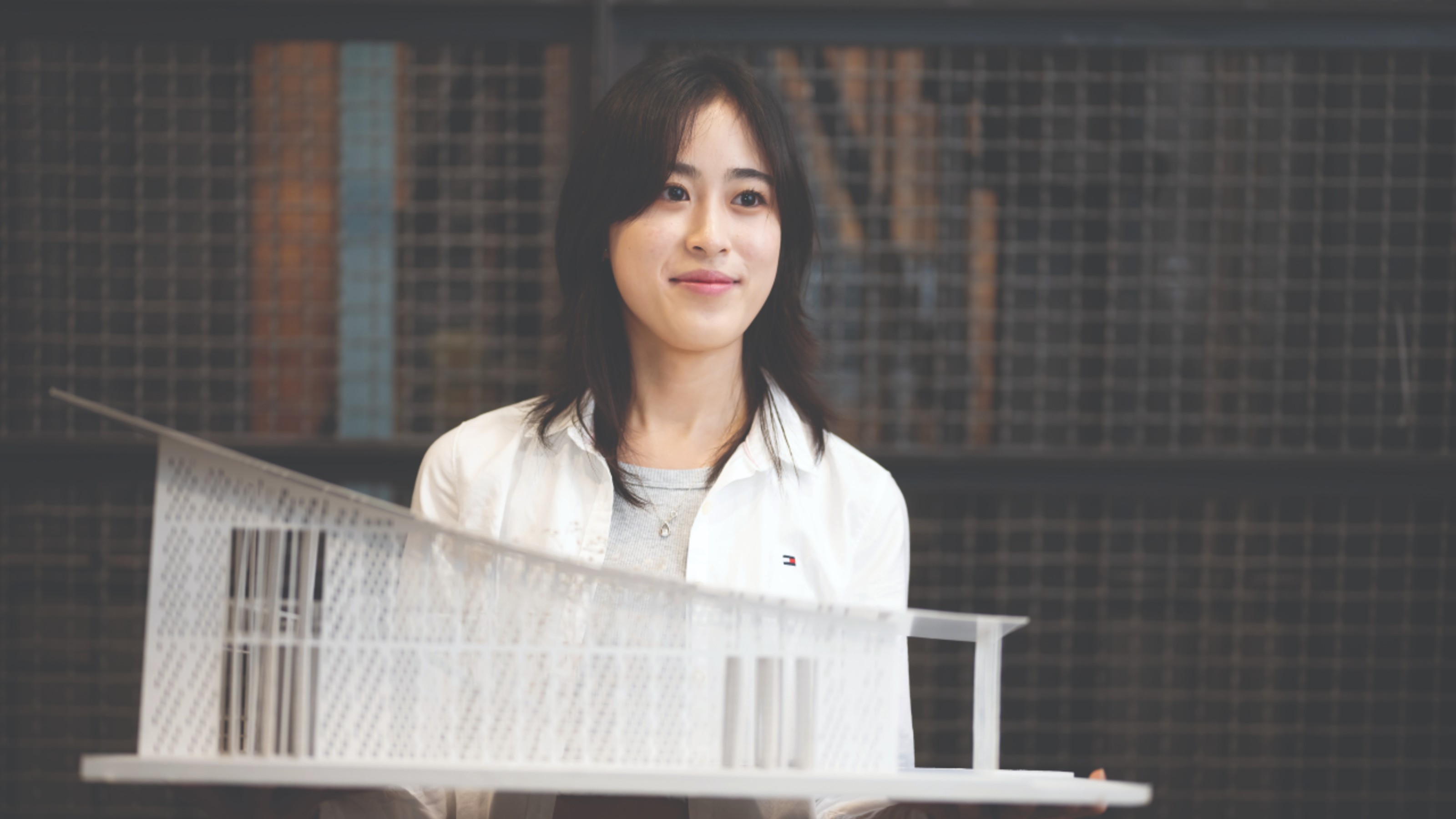 A student holding a model of a building they designed, the student is feminine.