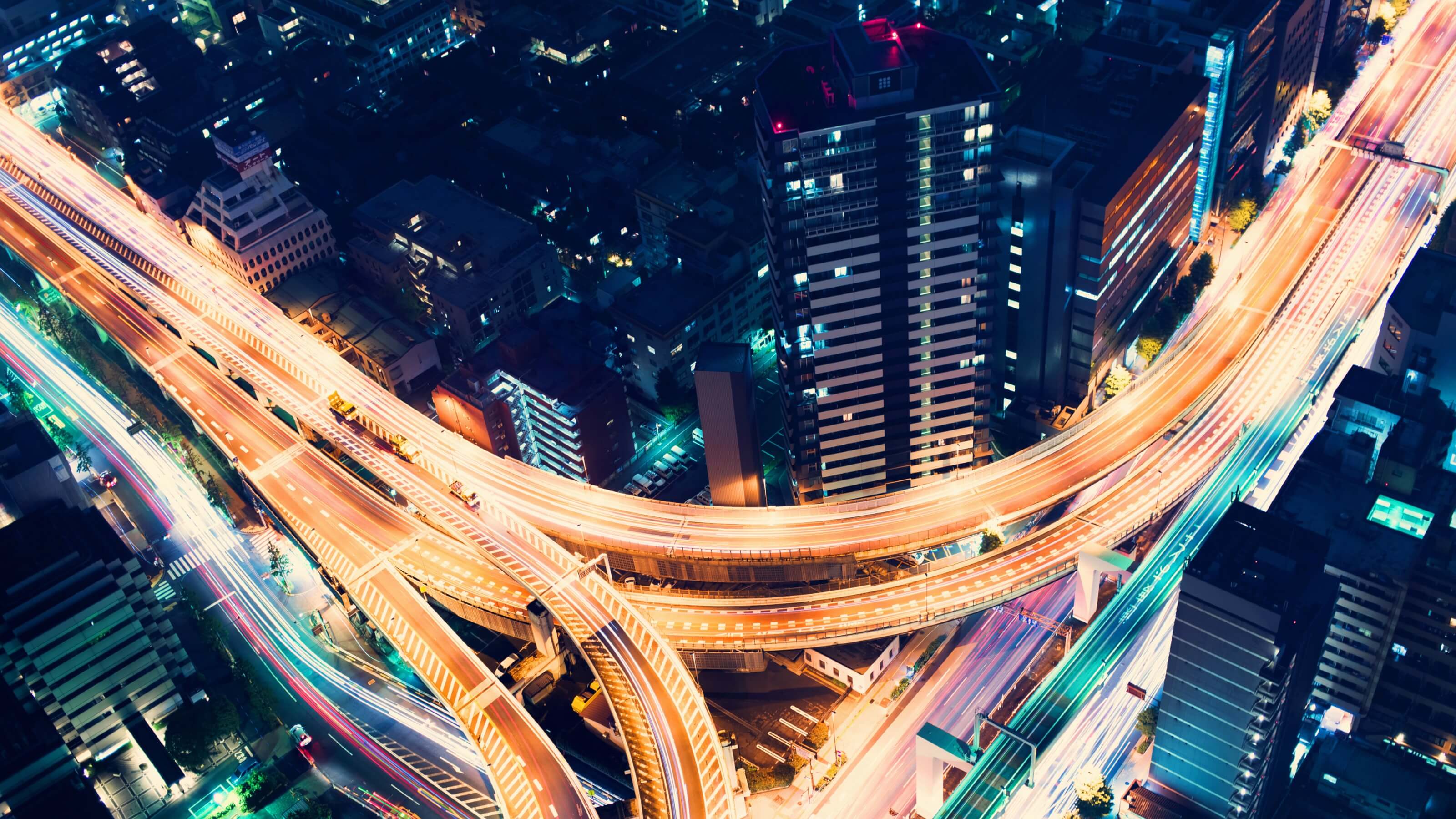 In image taken from above and looking down on a highway at night in a city, that glows orange under the street lights.