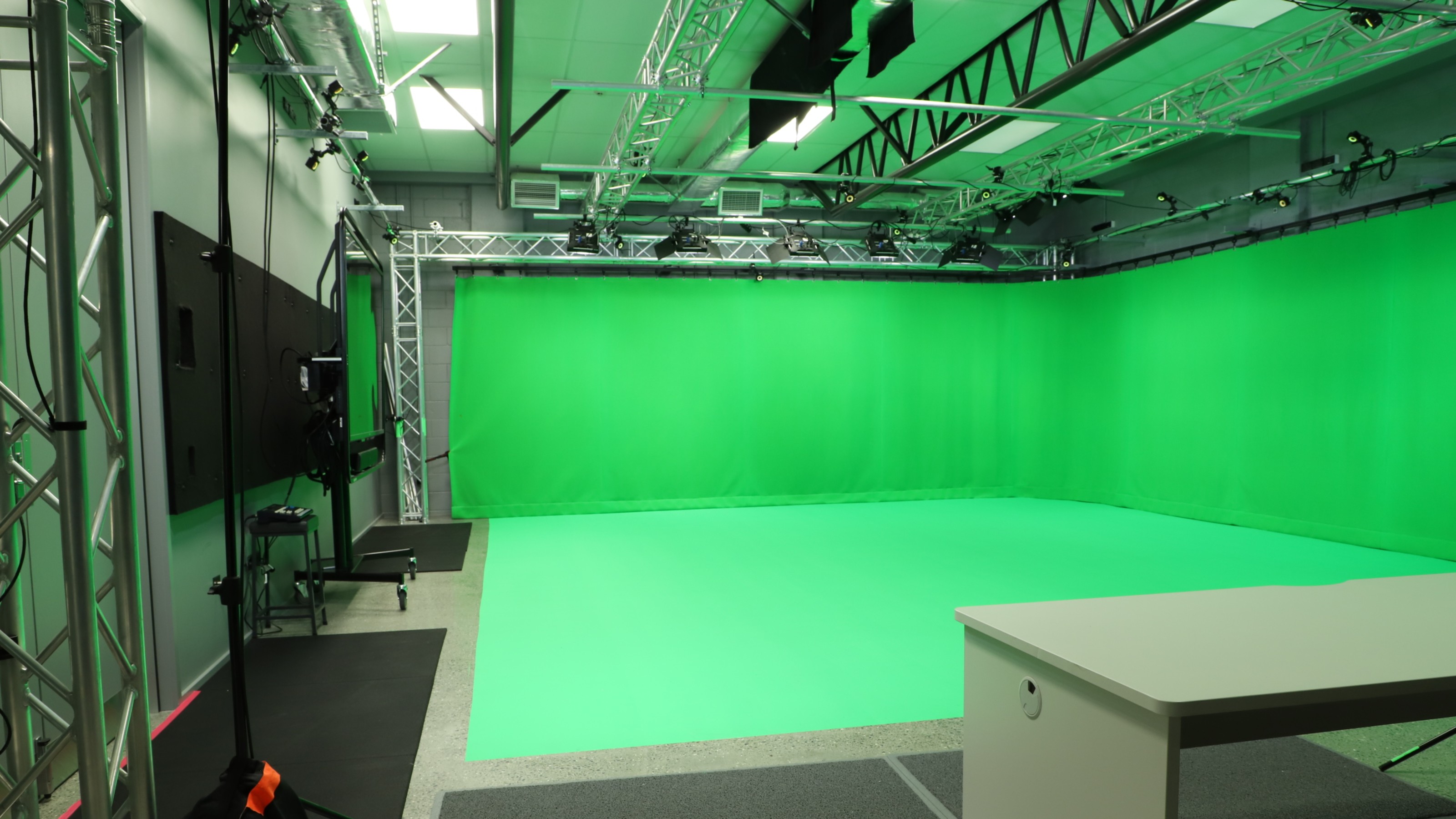 Studio with grey walls, green curtain, large screens.