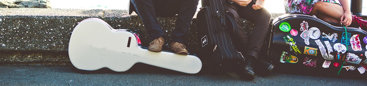 Banner - A close up image of a few guitar cases by the feet of musicians.