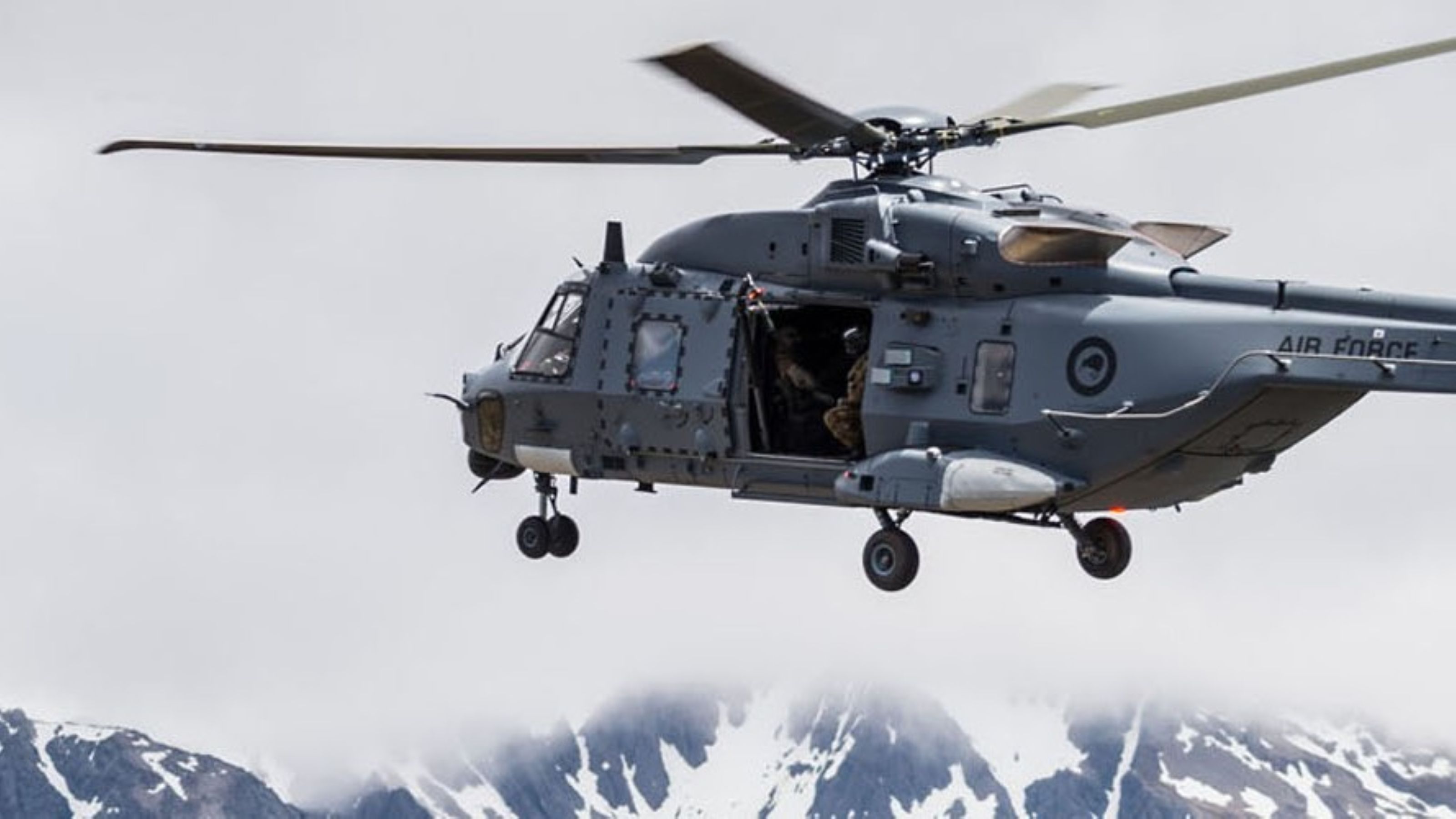 Military helicopter flying over snowy, cloud covered mountains