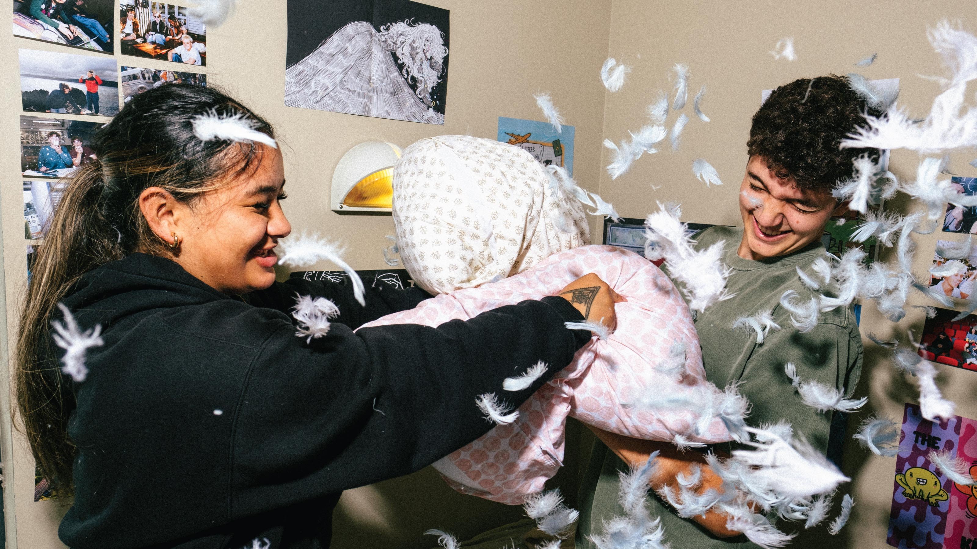 Two laughing students having a pillow fight with feathers flying