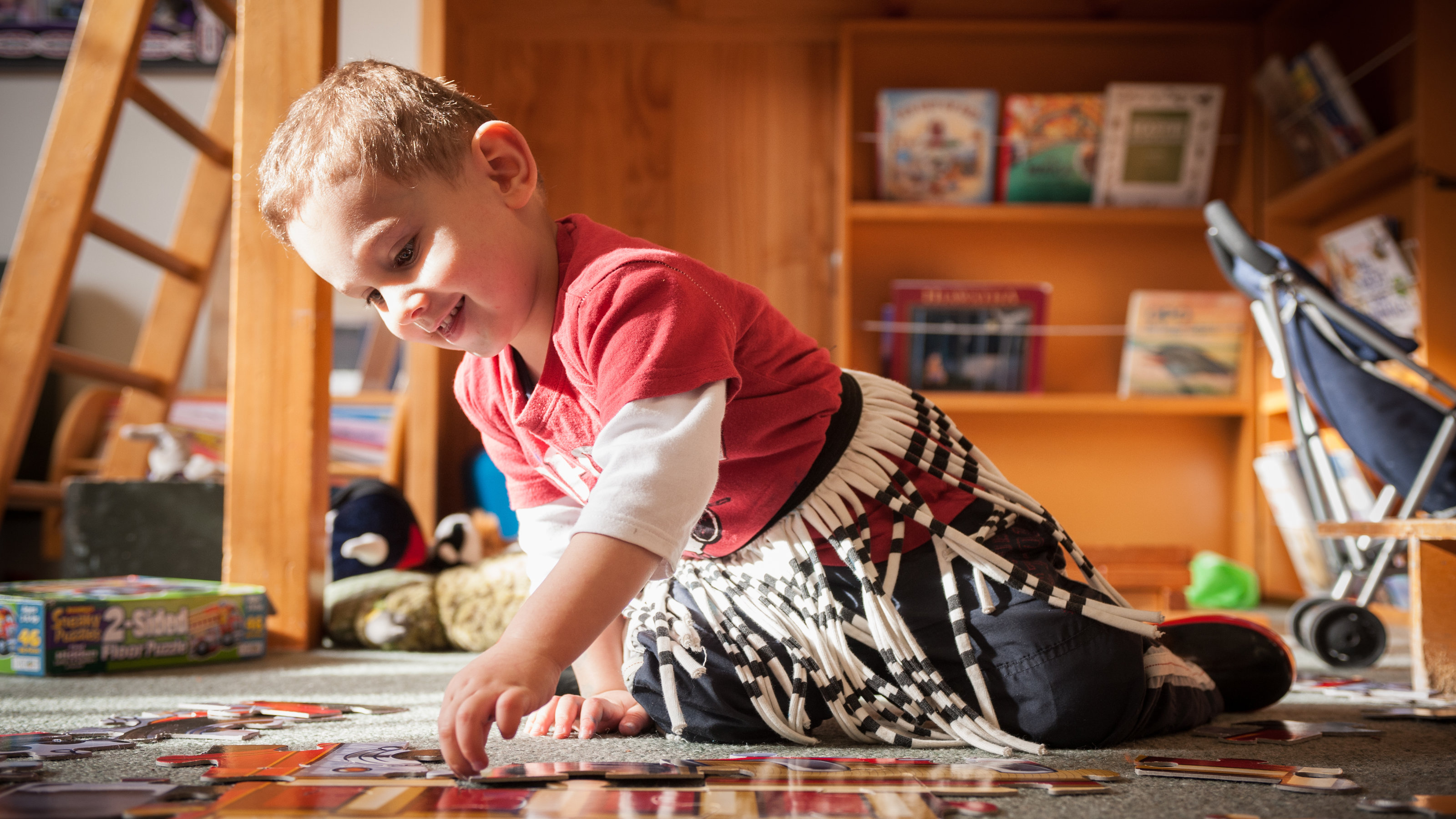 About Victoria Kids – A young boy smiles while playing with a puzzle on the ground.