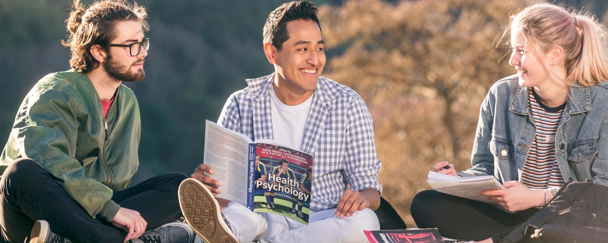 Three students sitting on a lawn and studying together on a sunny day.
