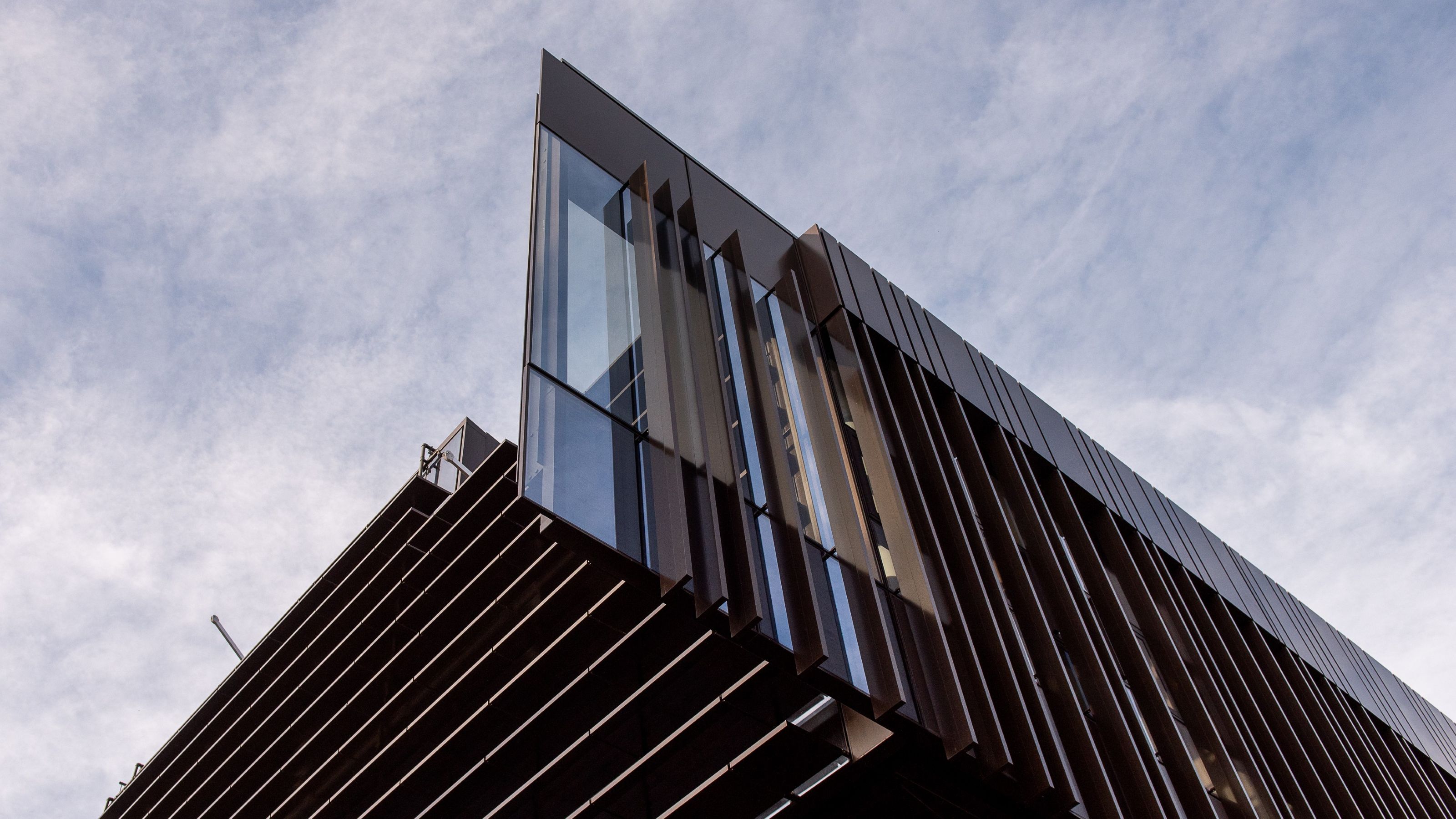 Close-up view of a modern building with angled glass and vertical metal fins against the sky.