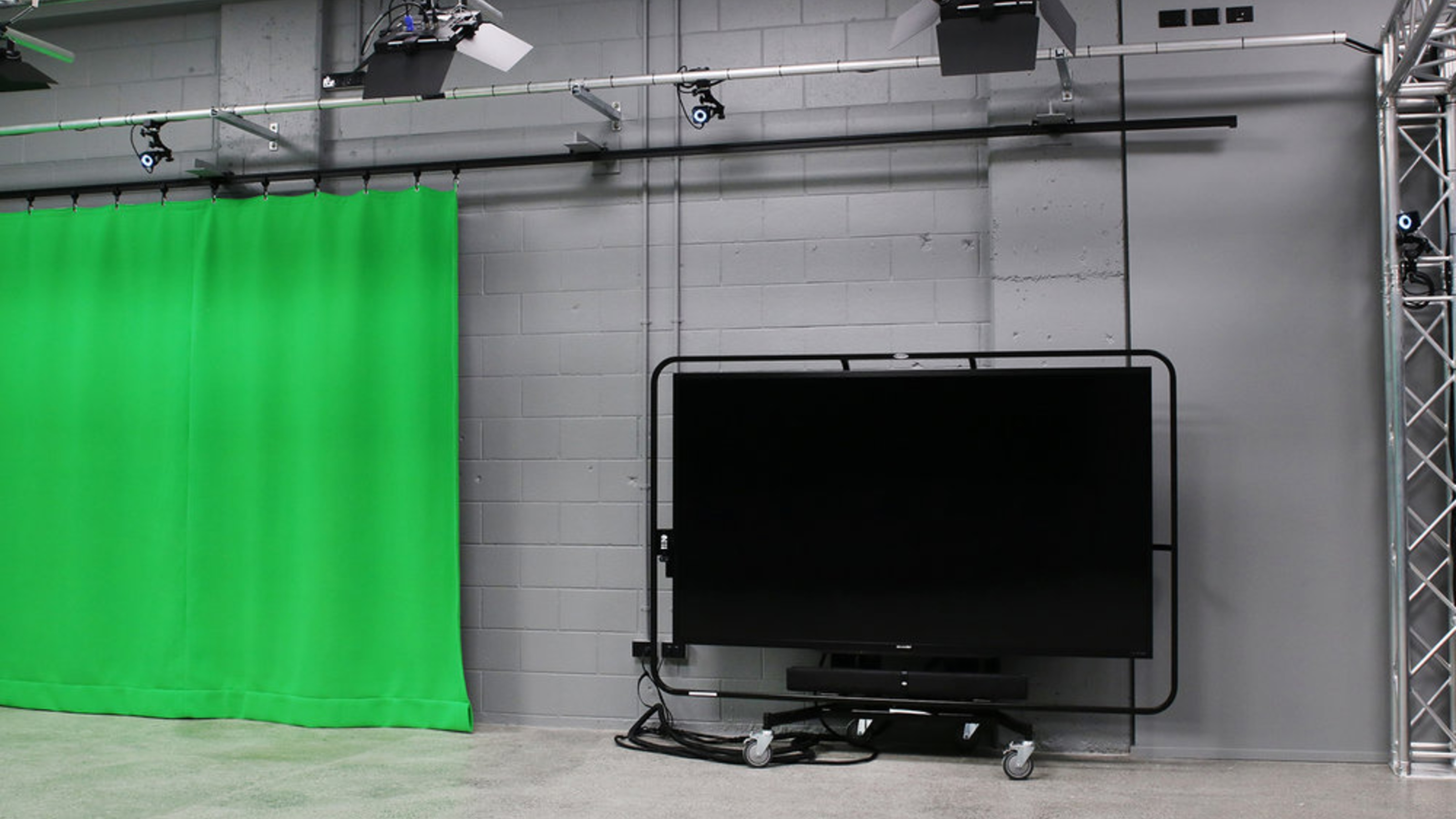 Studio with grey walls, green curtain, large screens.