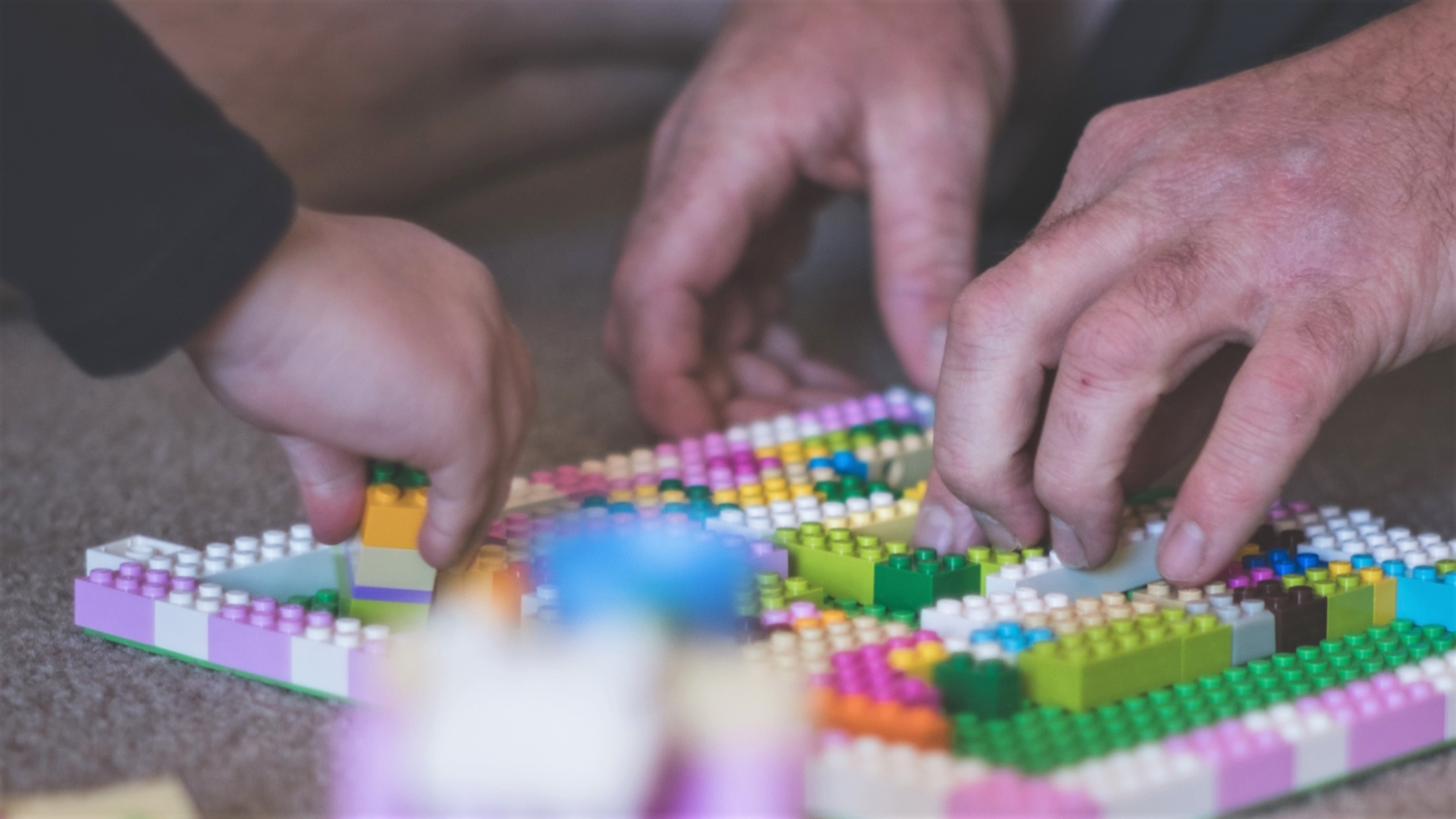 Close up of child's hand and man's hands playing with Lego pieces.