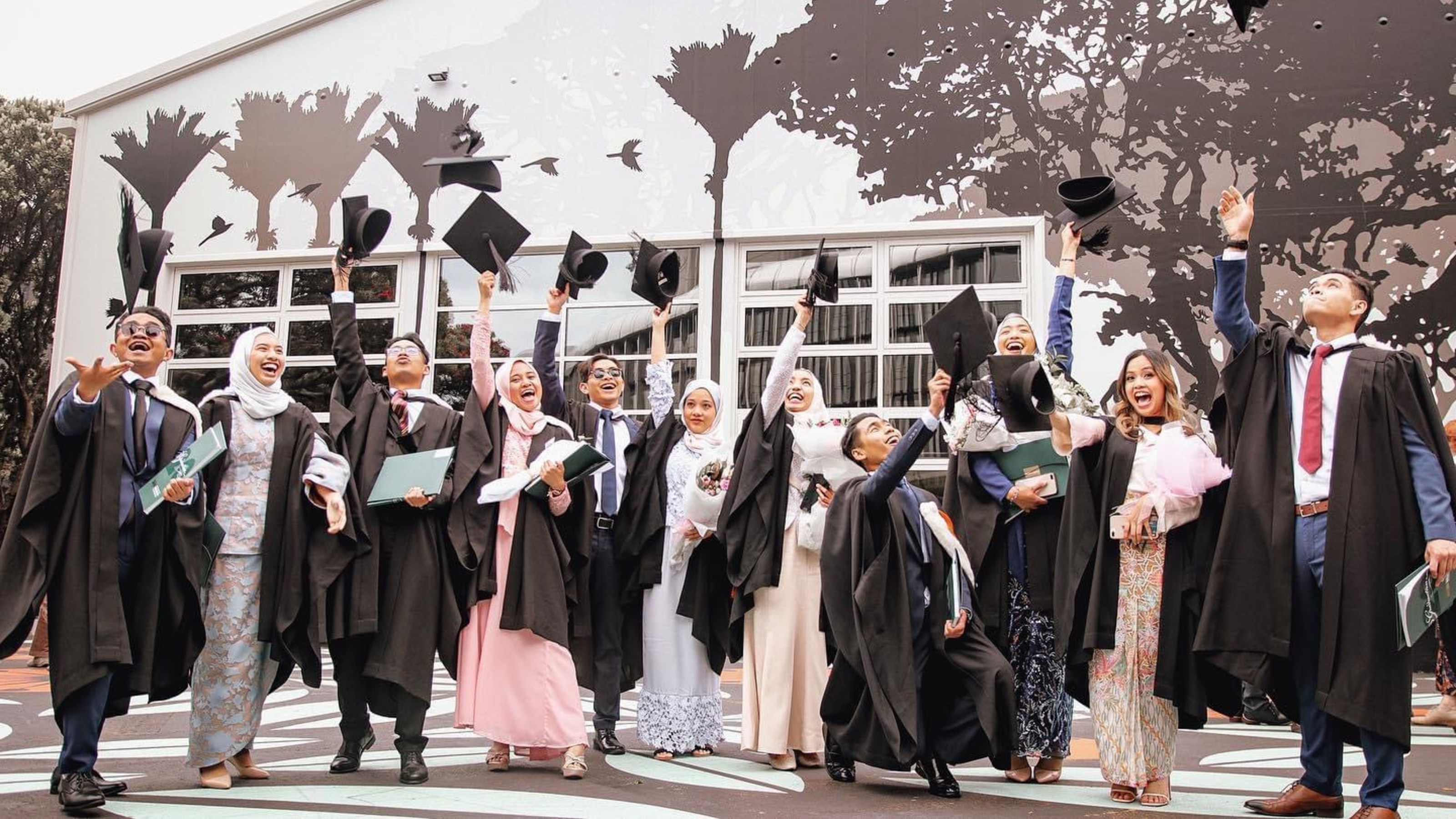 Malaysian graduates in academic dress, throwing their caps in the air.