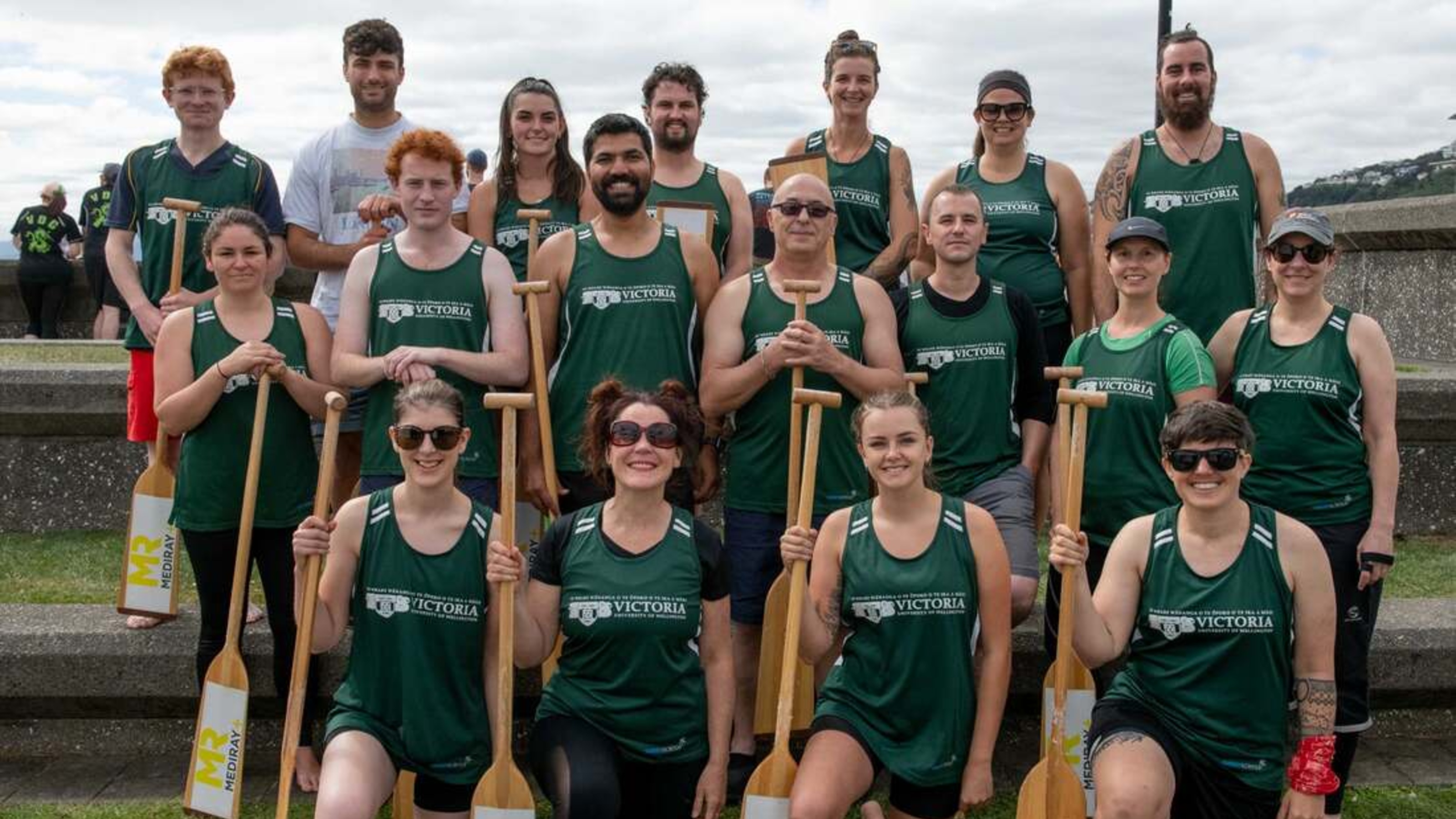 Dragon boating team wearing branded jerseys and paddles.