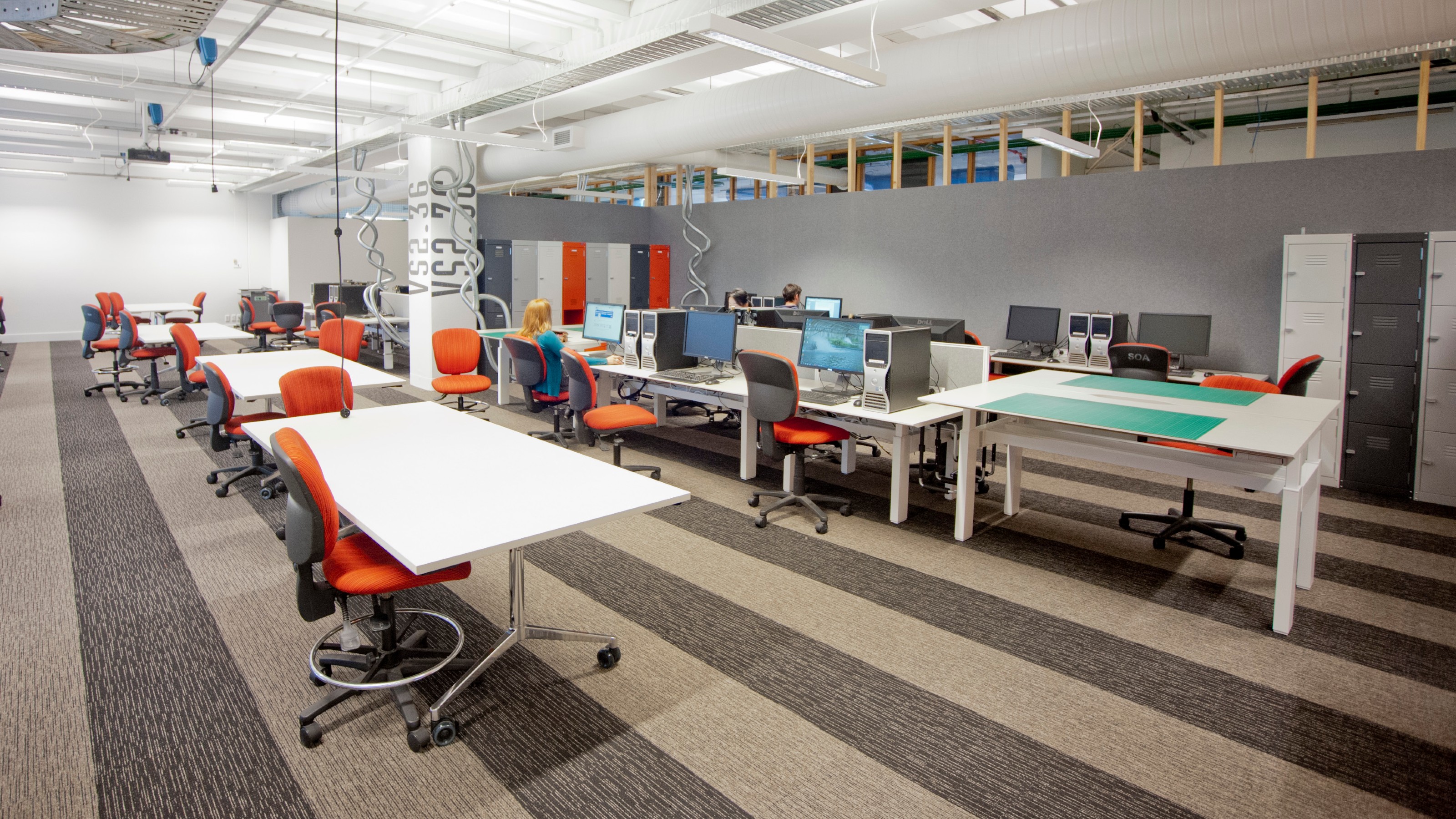 Wide shot of unoccupied work room with tables, chairs, and computers, with windows in background