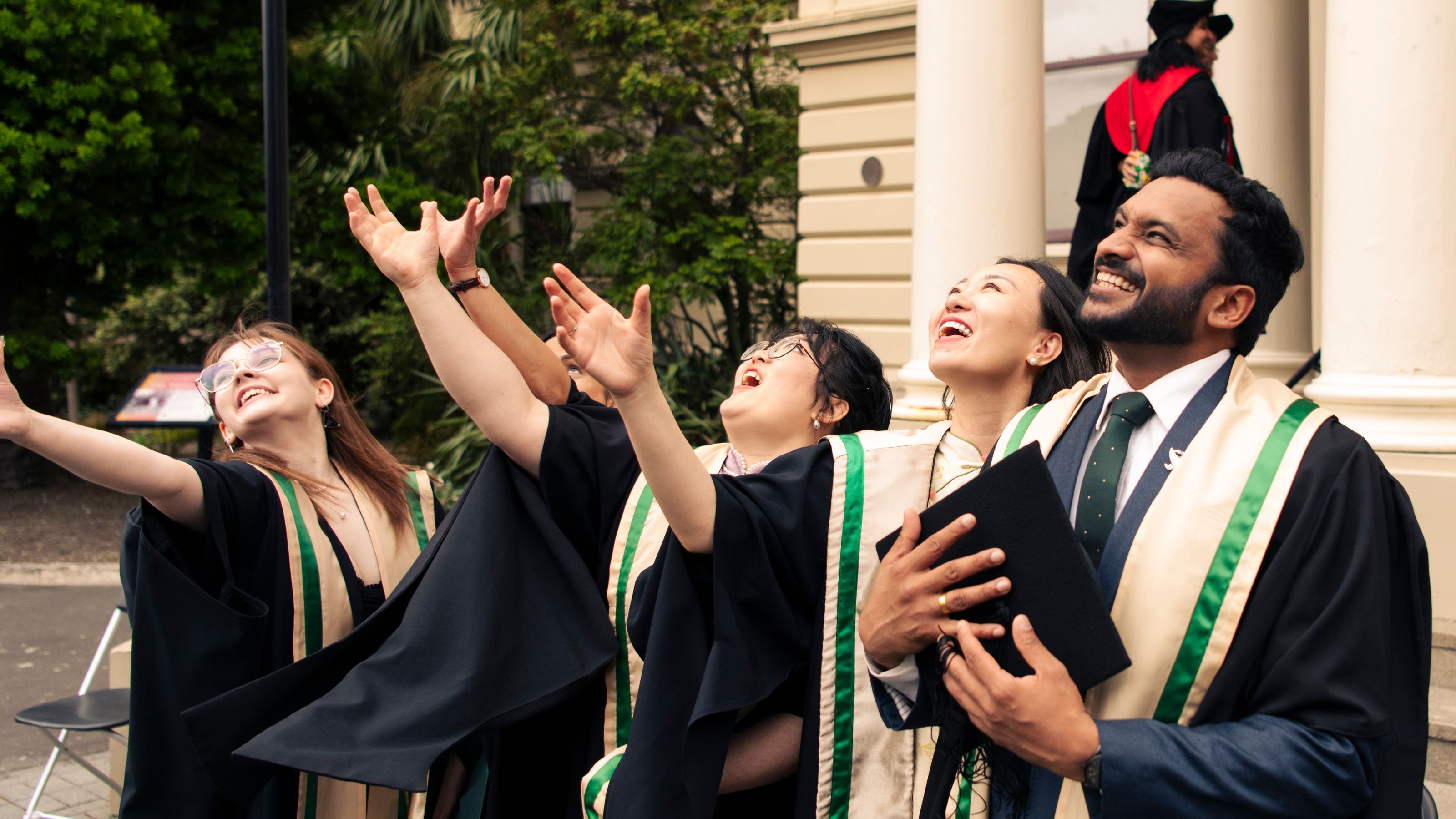 A photo of a group of students in graduation gowns smiling and throwing their caps.