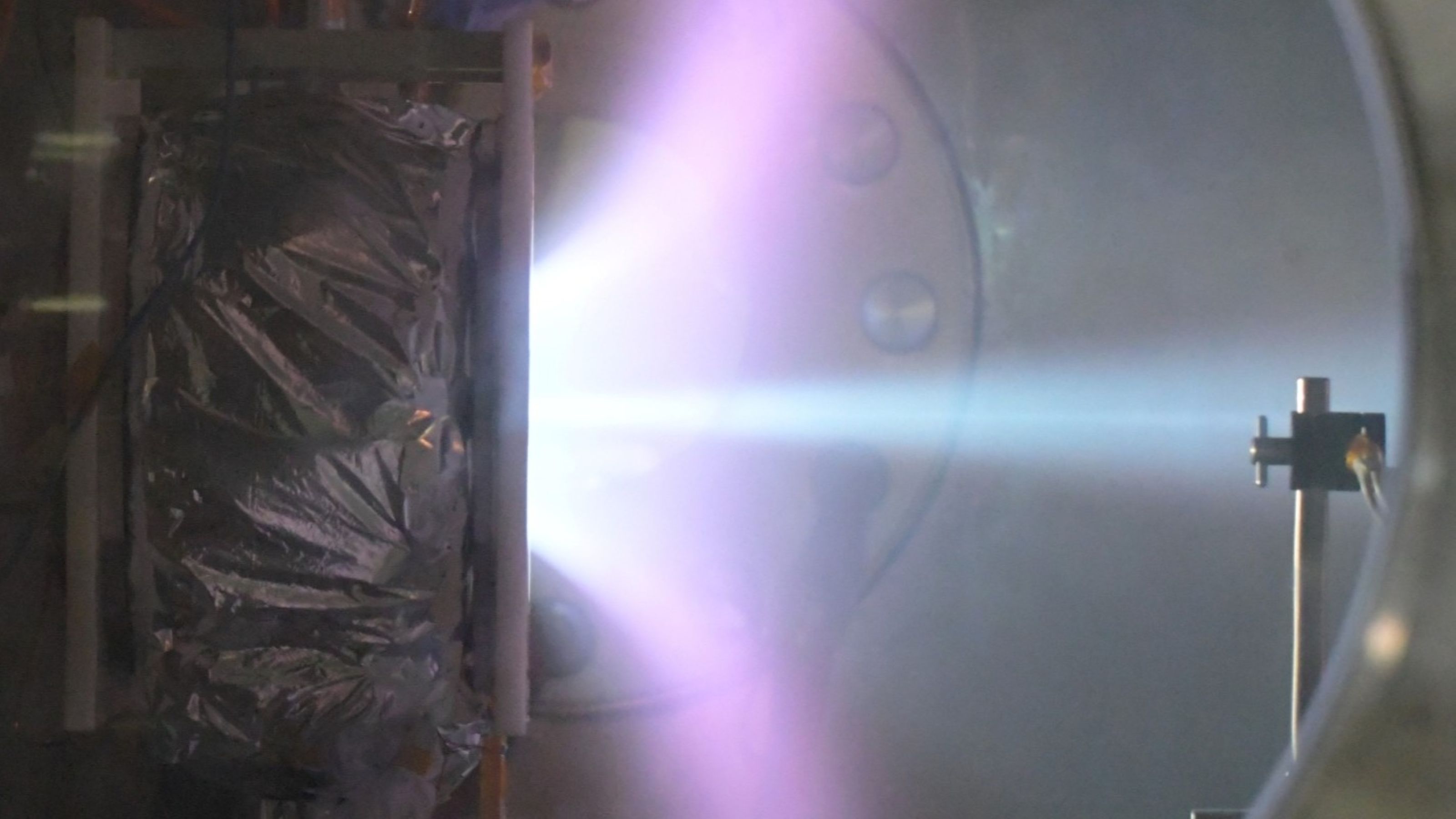 Purple-blue plasma plume inside a laboratory vacuum chamber.