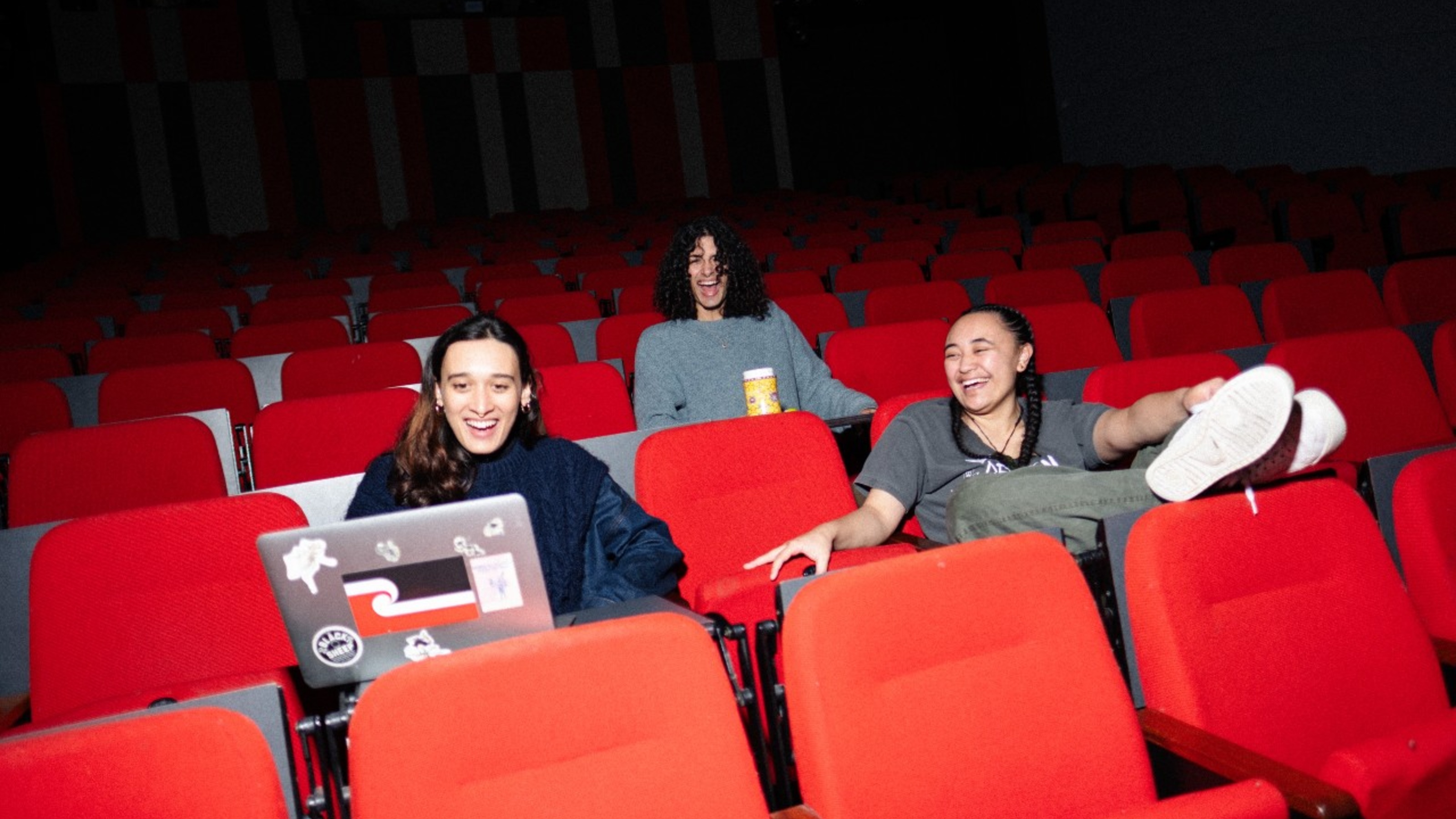 Students laughing and looking at a laptop in a cinema.