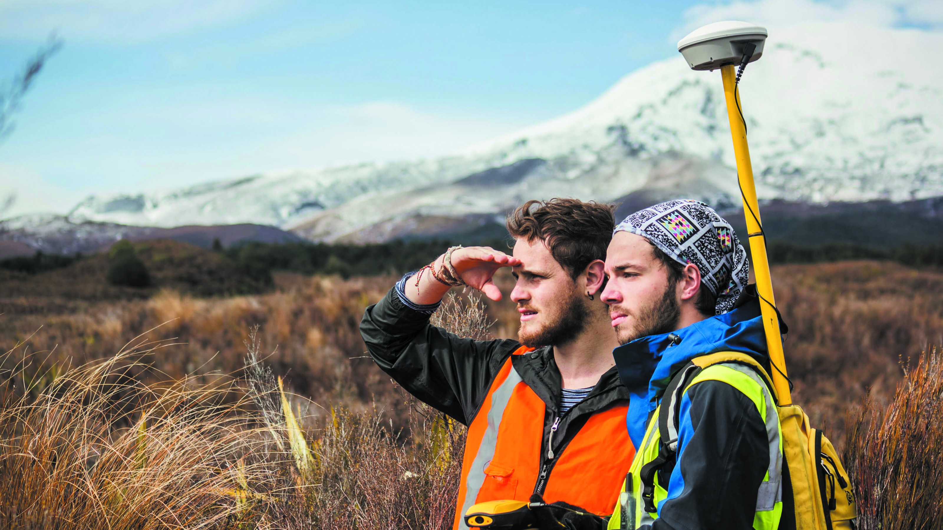 Two students with safety gear, standing in front of a snowy mountain