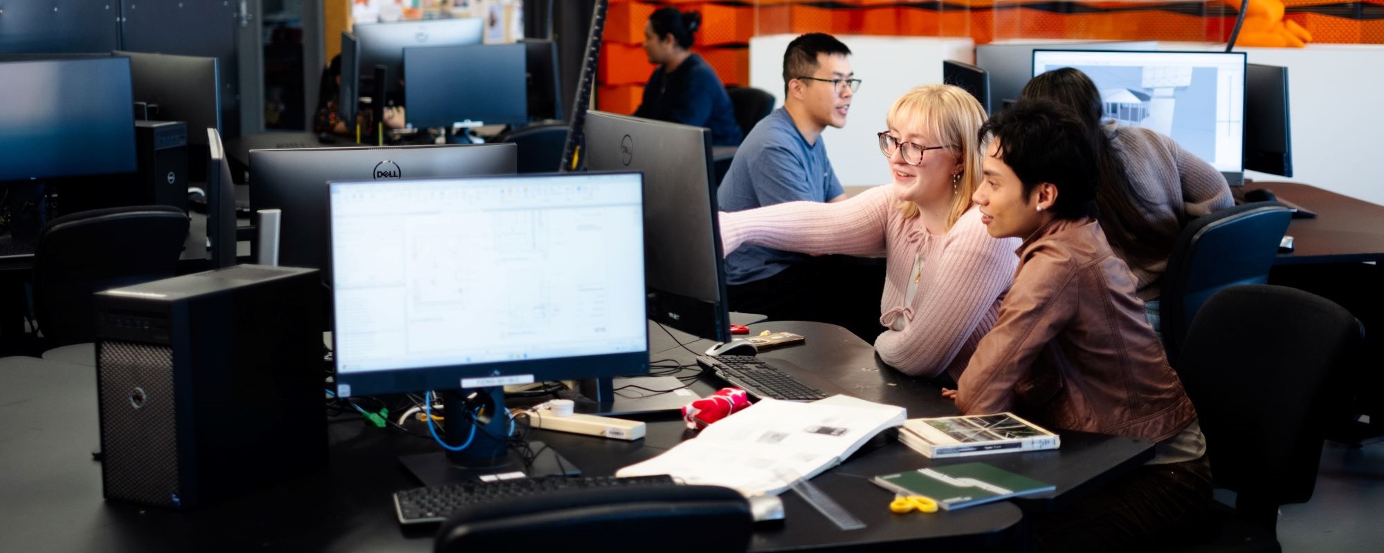 2 students sitting side by side at a computer. 1 student is pointing at something on the screen.