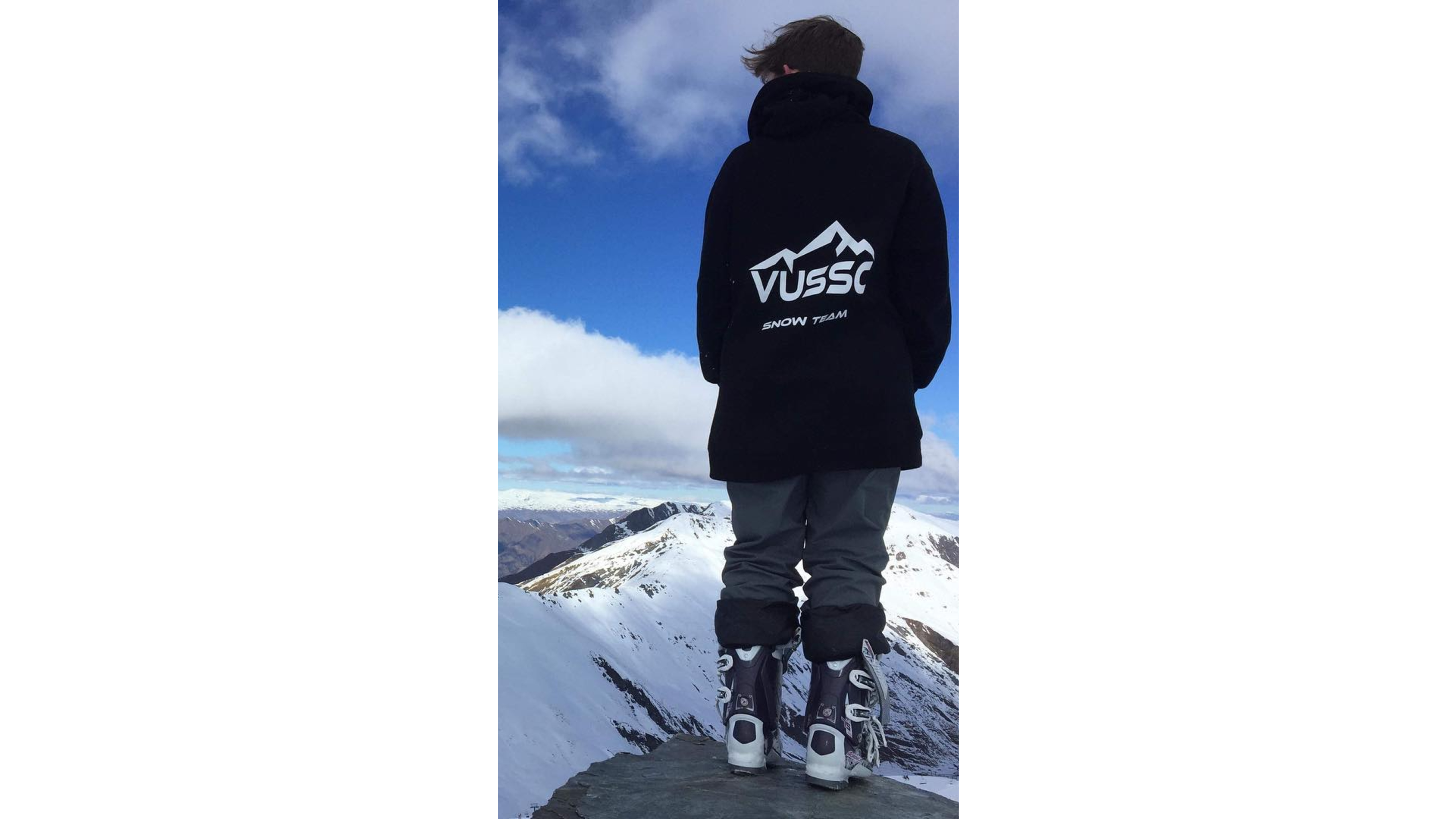 Student standing on rock, facing mountains, wearing hoodie saying 'VUSSC snow team'.
