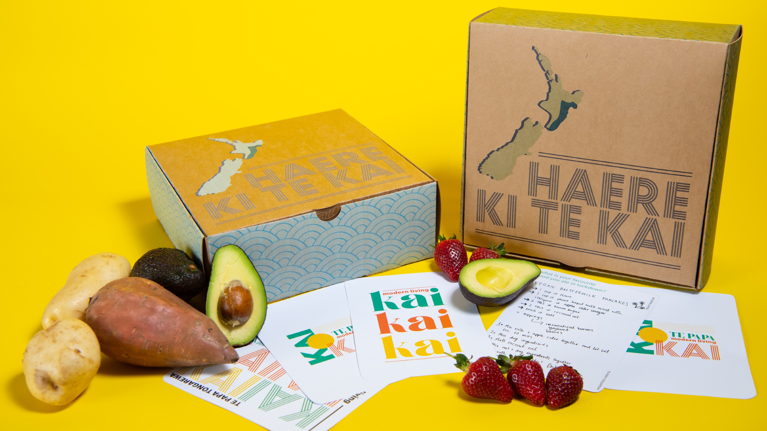 Cardboard box featuring map of New Zealand surrounded by fresh vegetables, and colourful cards that say kai