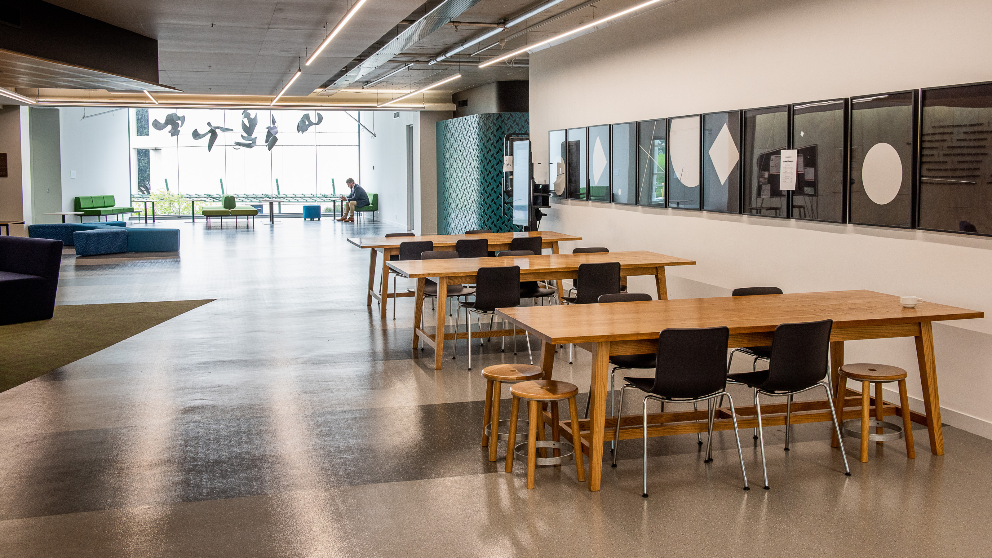 Mezzanine space at Rutherford house with three tables with chairs in foreground, soft seating ont eh left of teh image, and student on couch in background.
