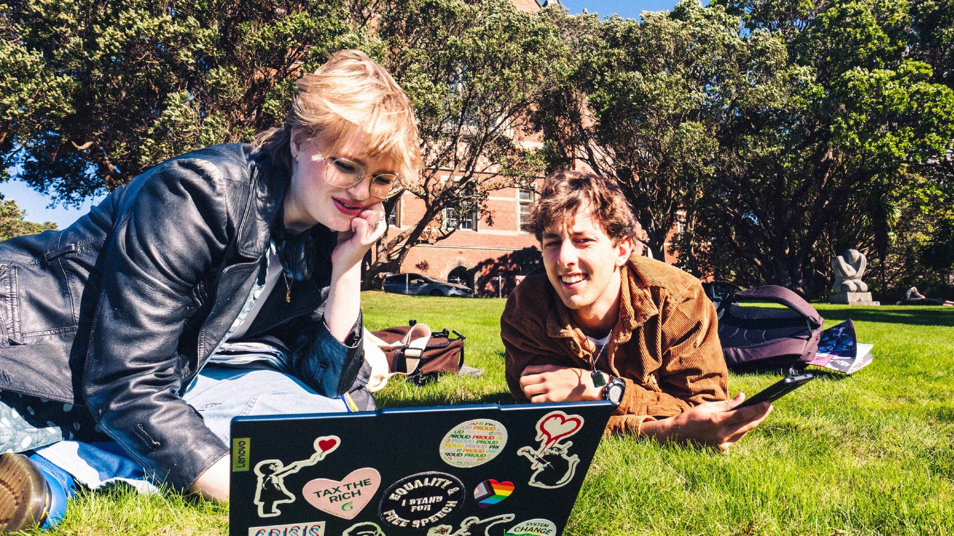 Students looking at laptop and sitting on the grass