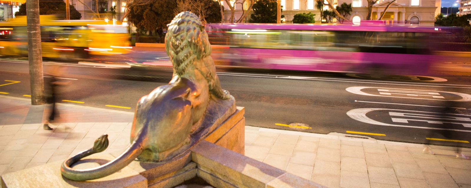 Looking from behind a lion statue across the road at dusk, with the Old Government Buildings in the background