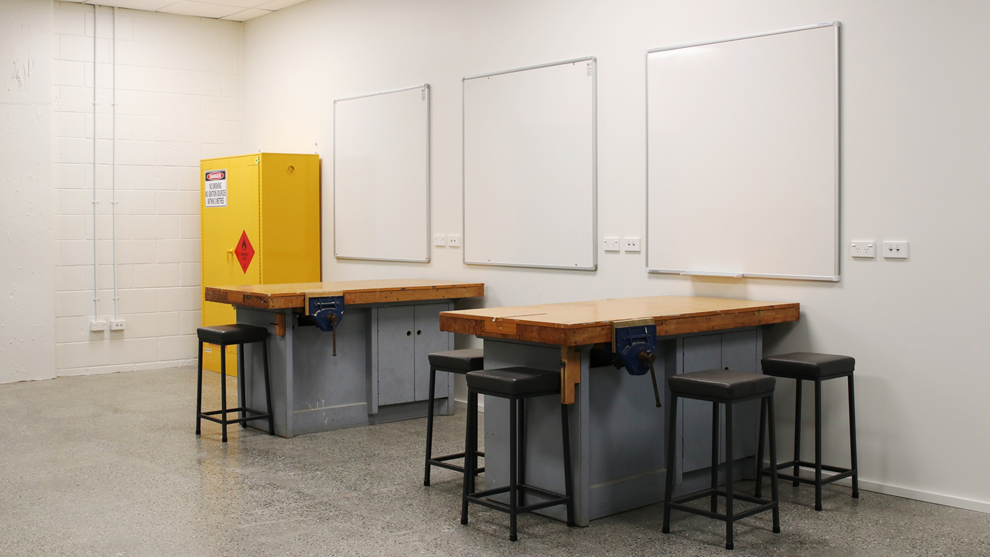 Workshop with white walls, bright light, and high working tables and stools.