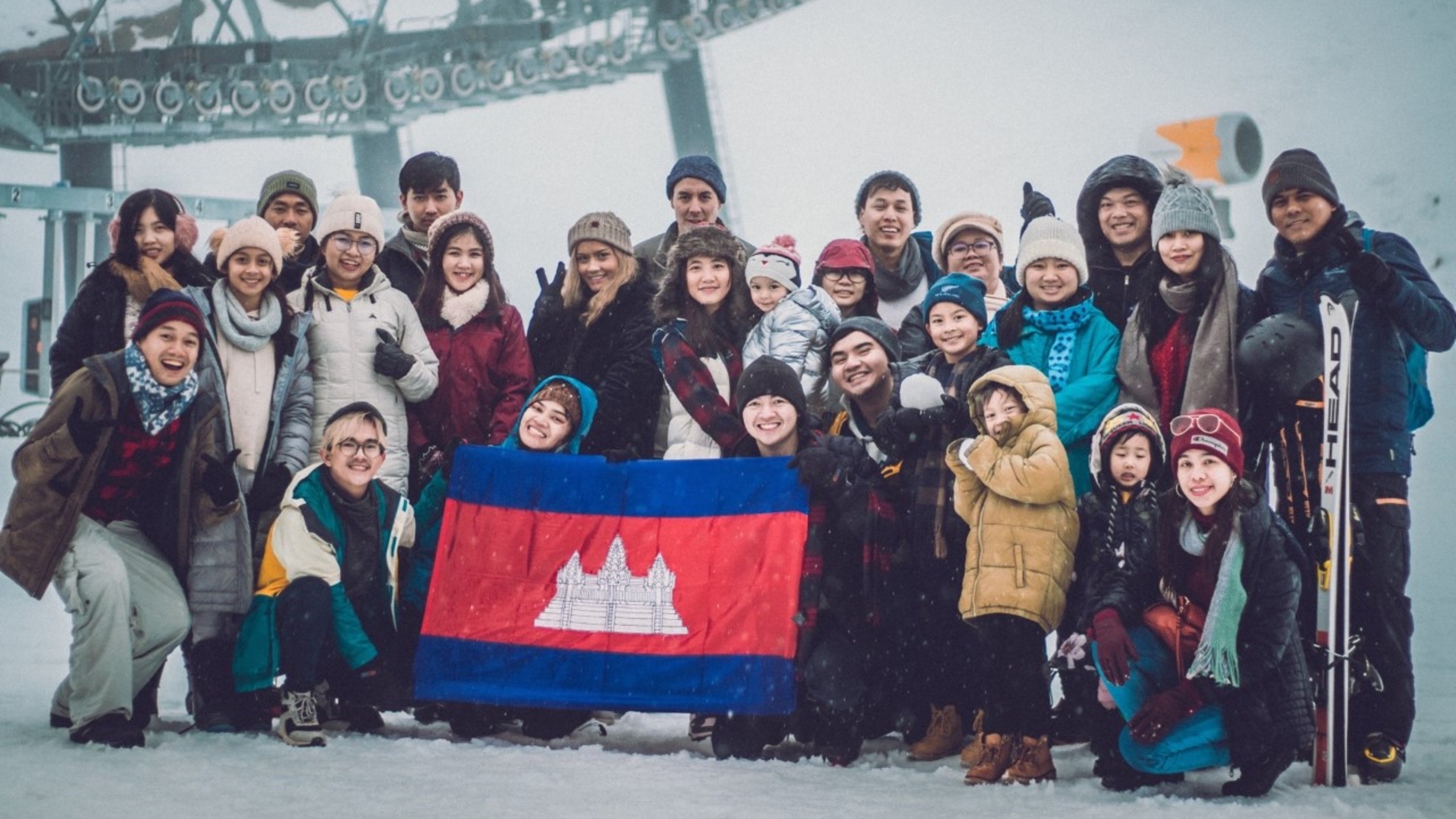 Cambodian students and their families on a trip in the snow holding up a Cambodian flag.