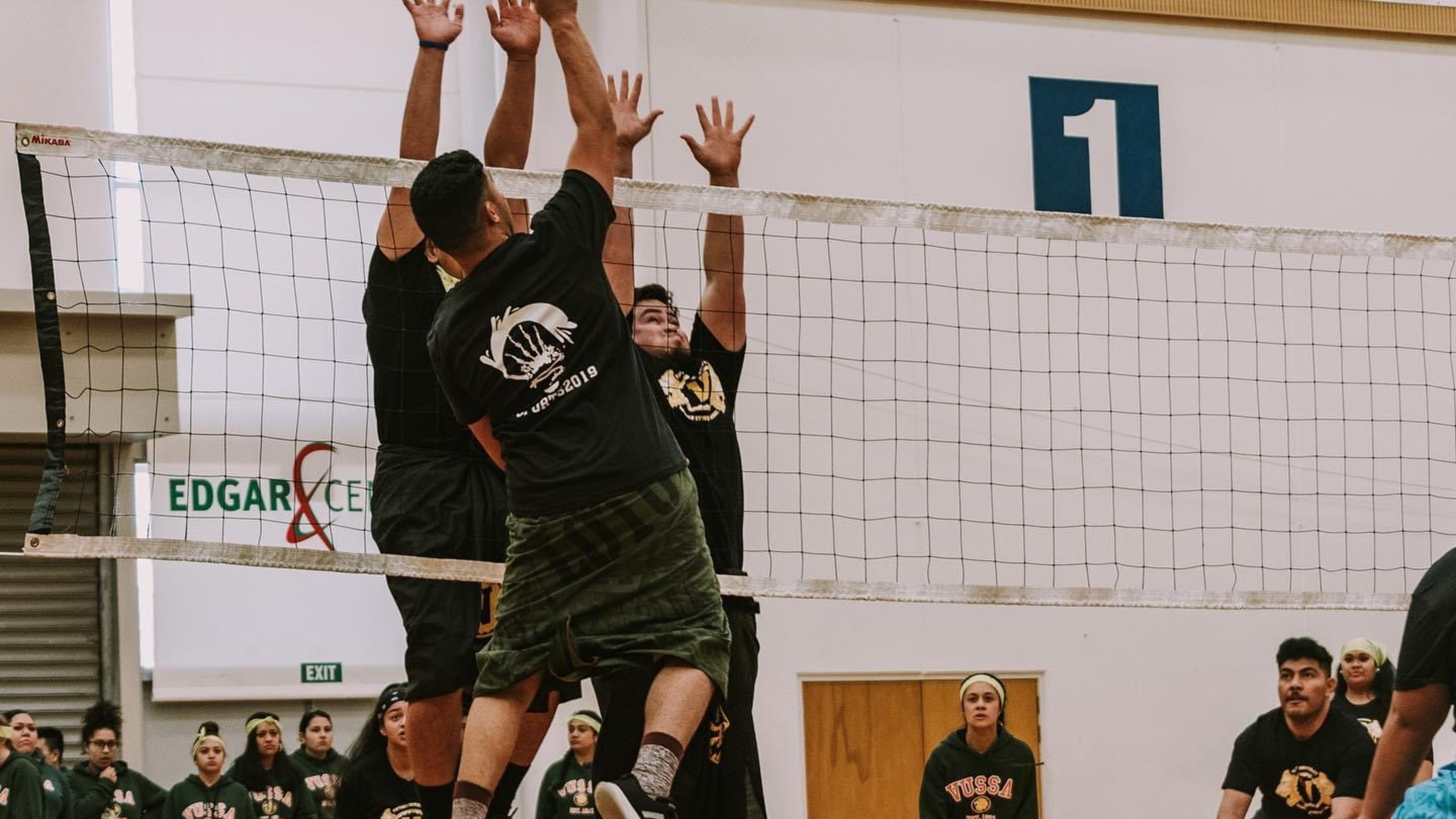 Volleyball players jumping to reach the ball by the net.