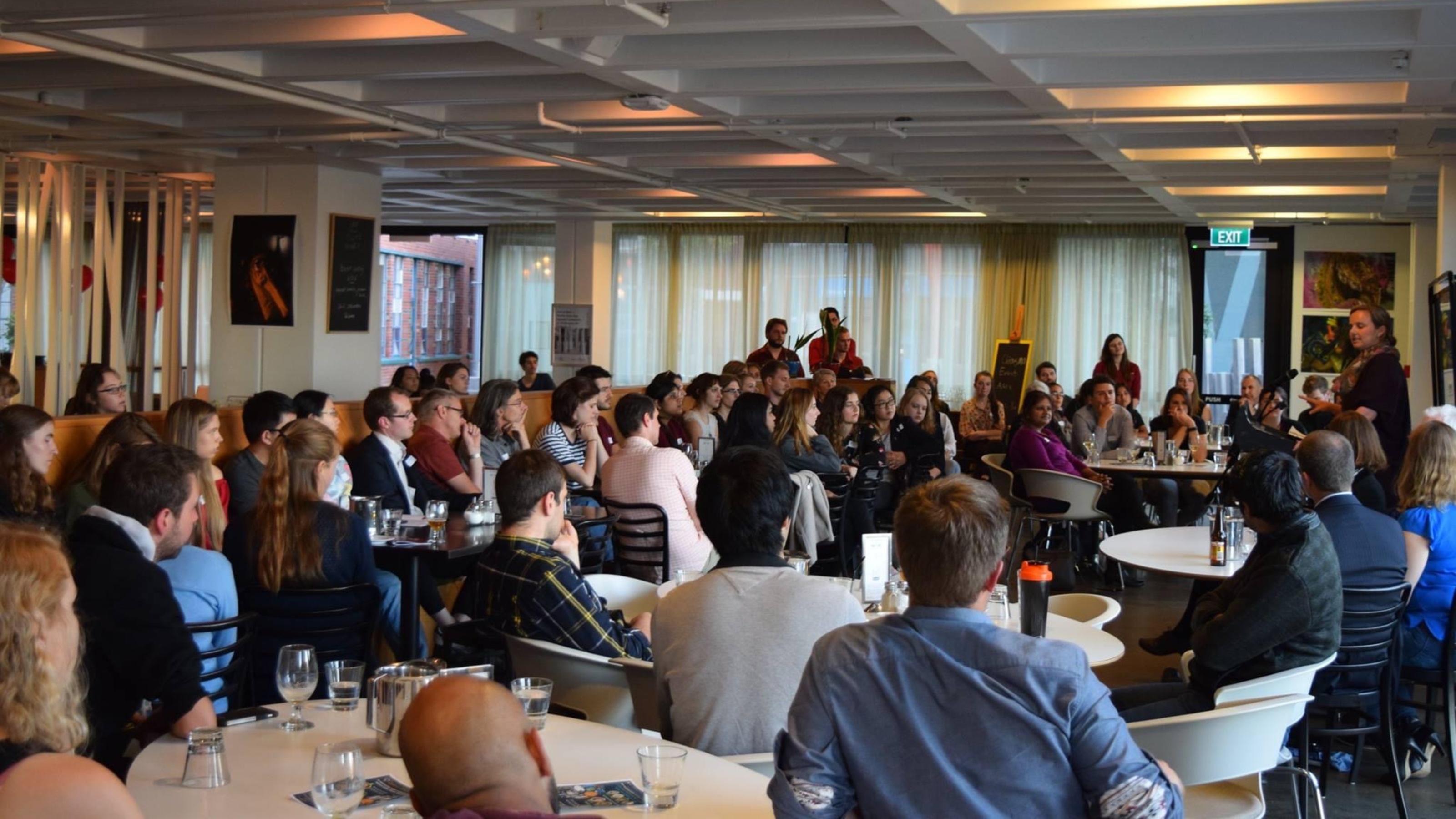 Crowd of people sitting at bar, listening to speaker, during Chiasma event.