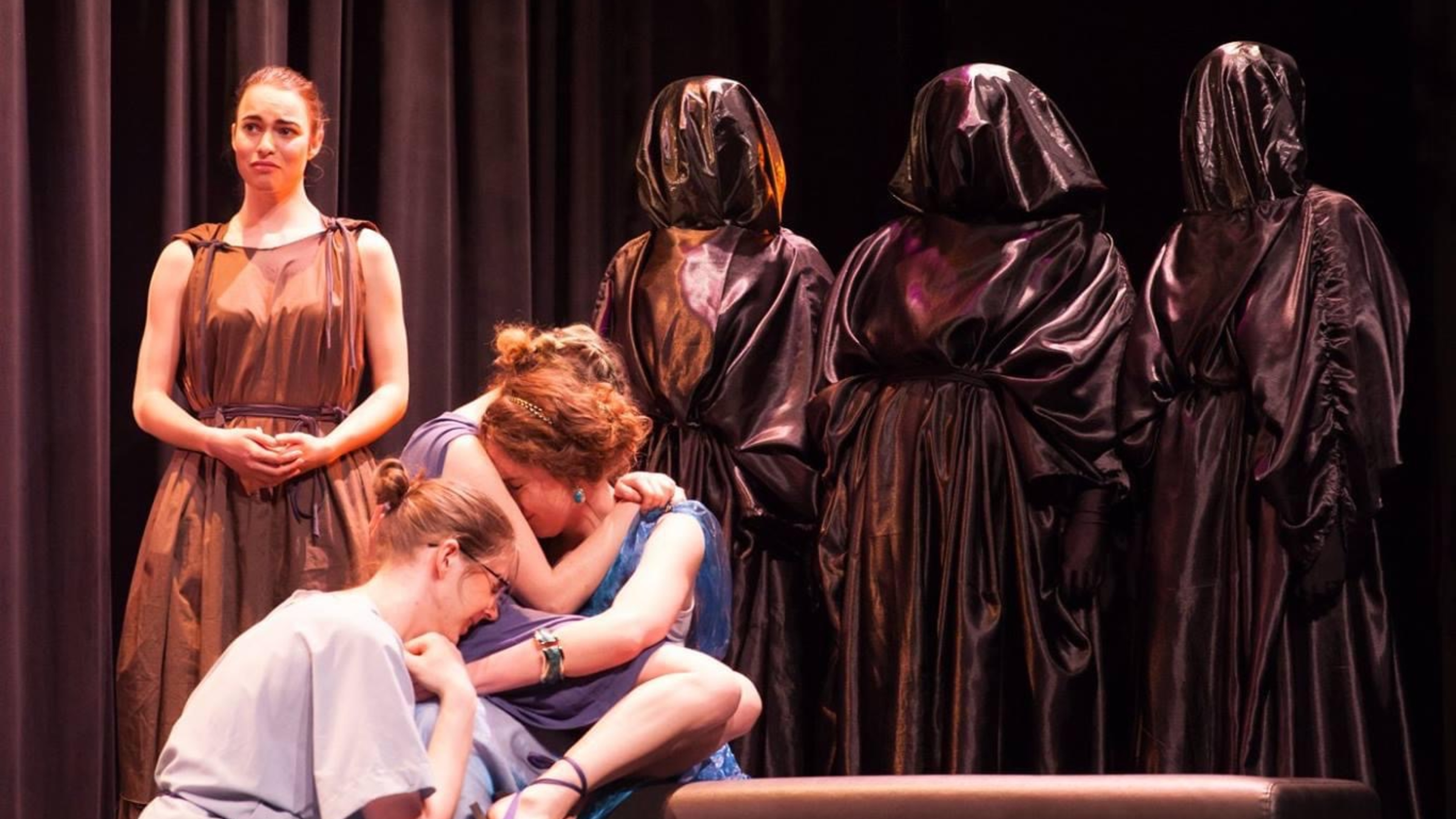 Performance with three crying actors, three figures covered in black cloth, and one narrator in brown toga.