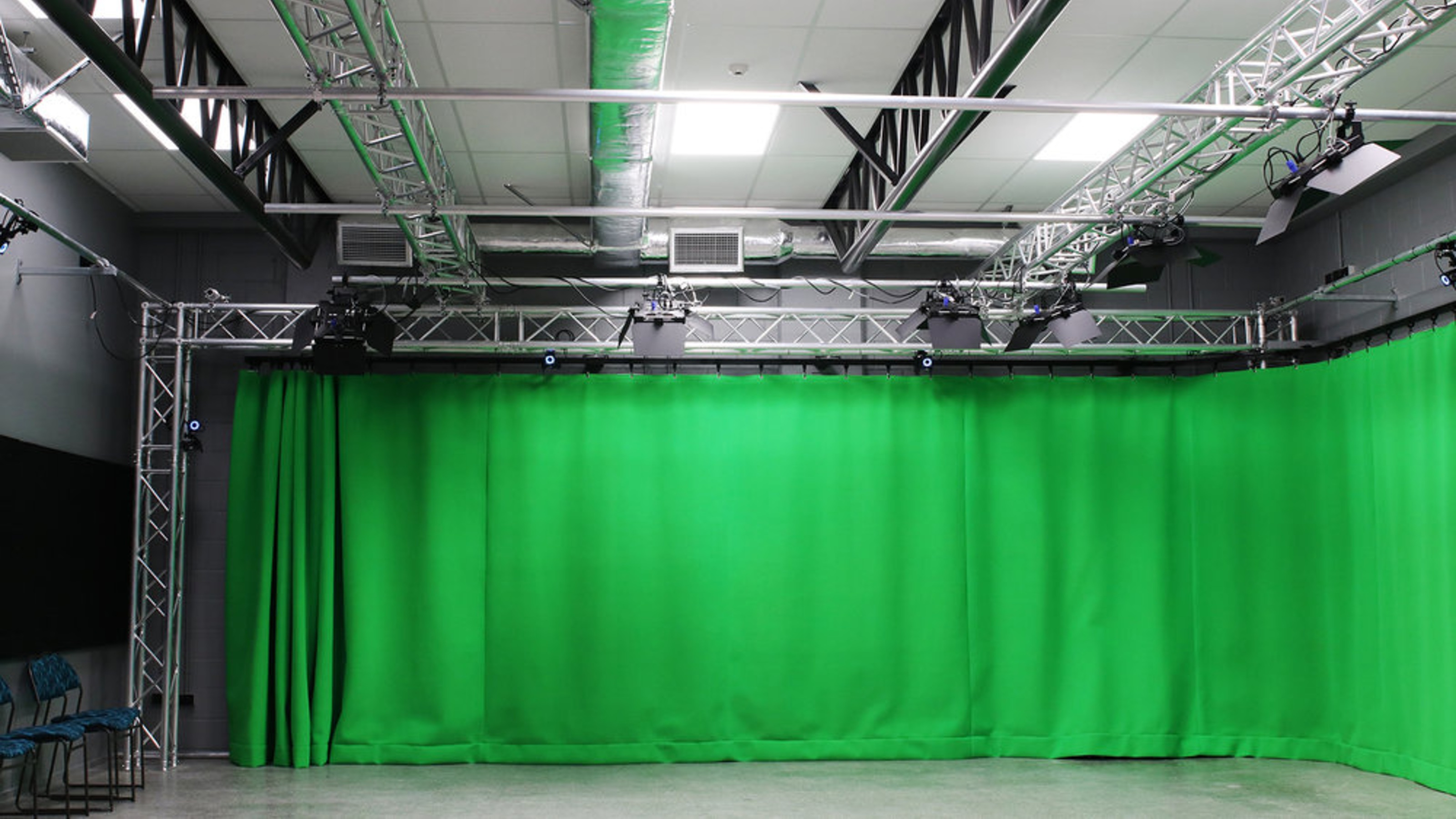 Studio with grey walls, green curtain, large screens.