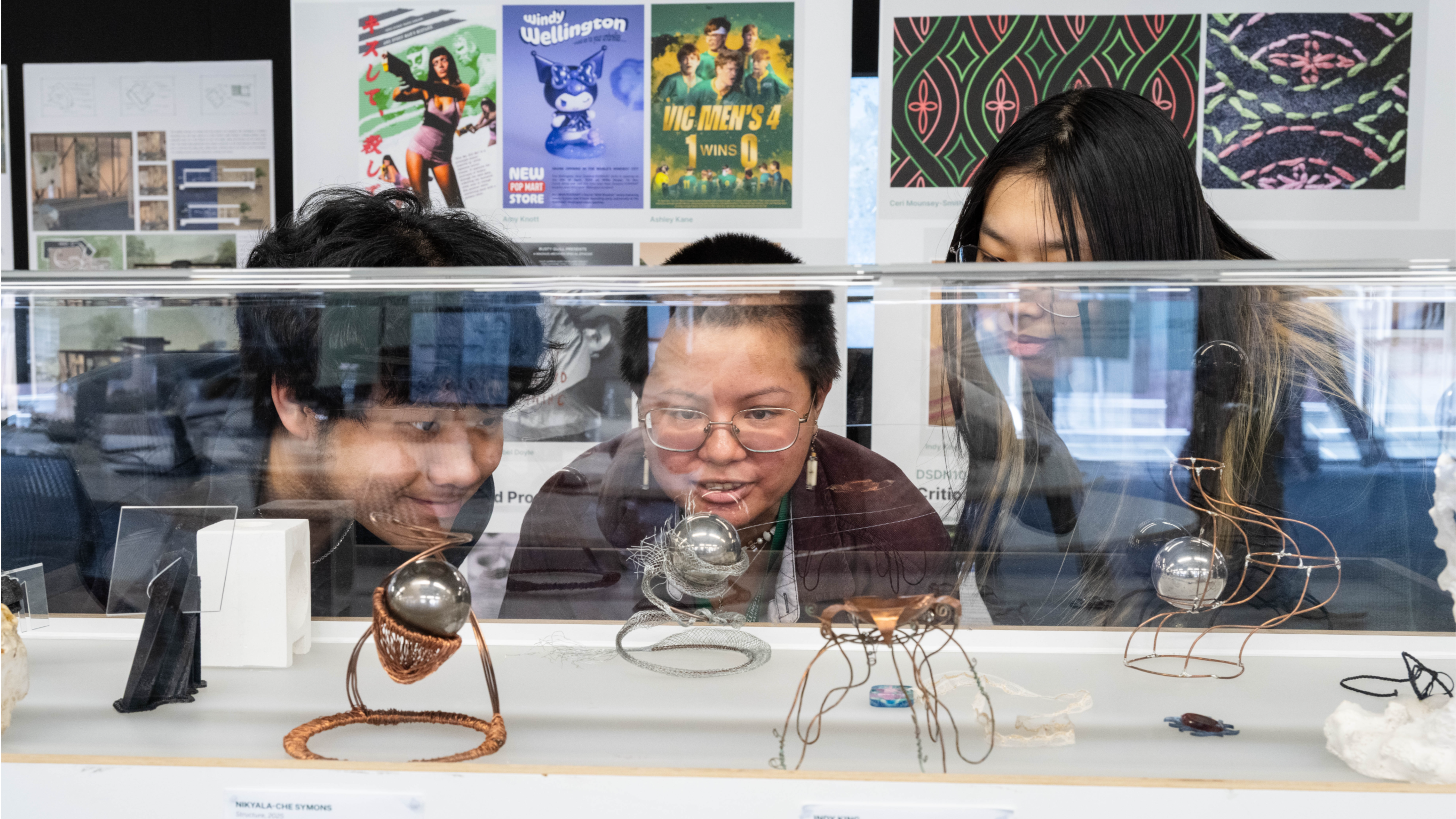 Three students observing student works in a vitrine
