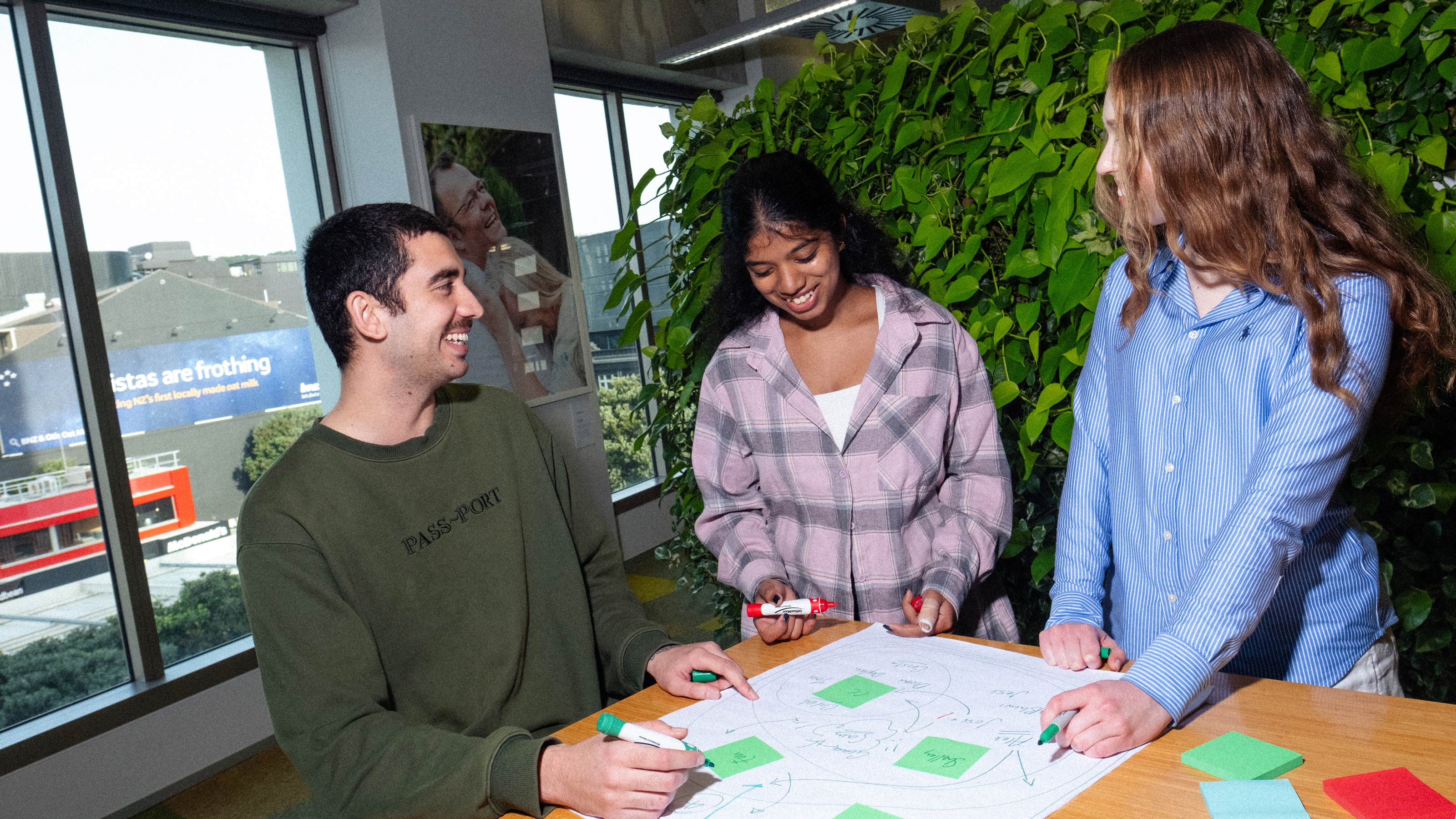 Three students brainstorming at a table with pens and sticky notes