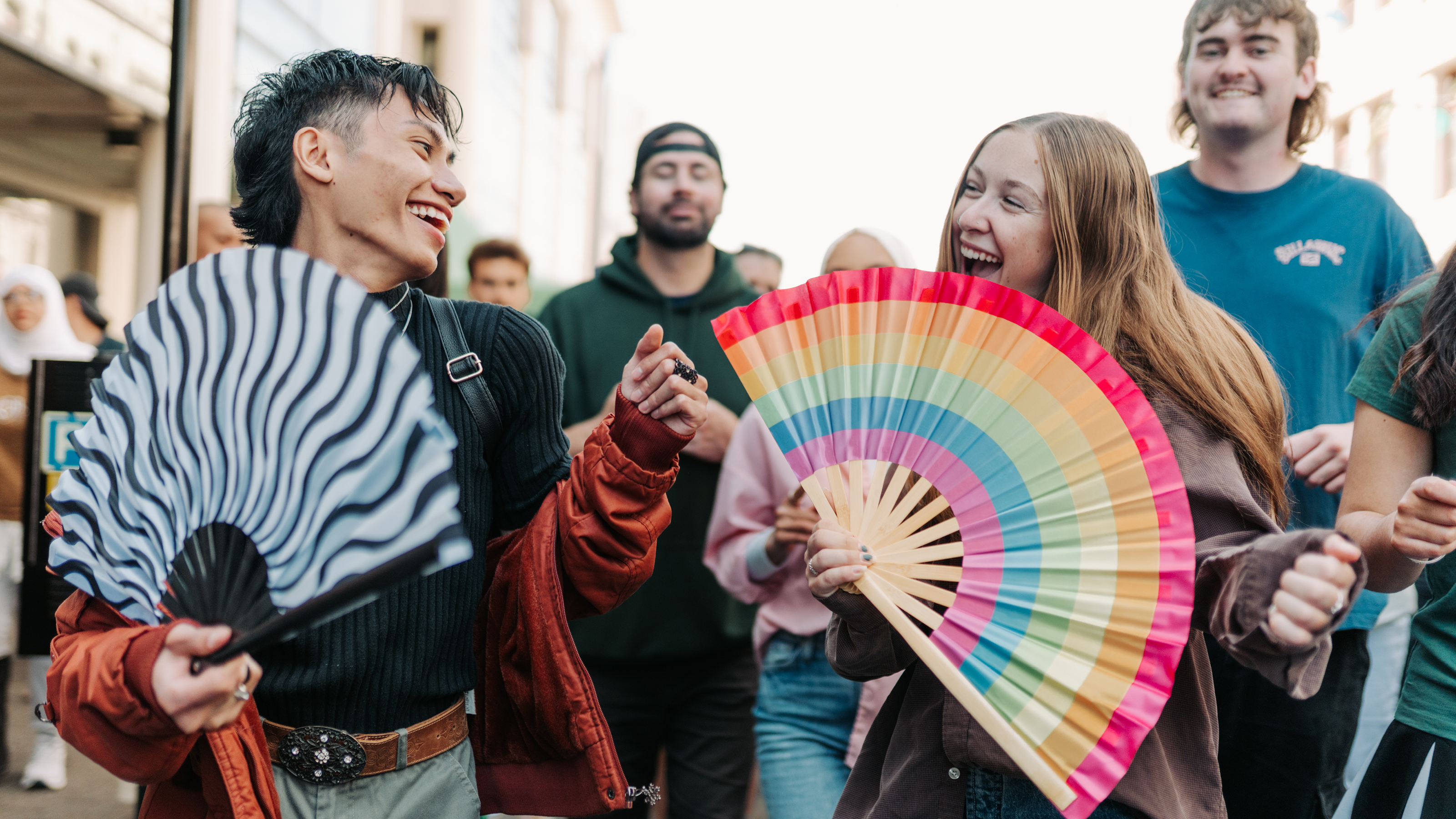 Two students in the street with a colourful rainbow fan