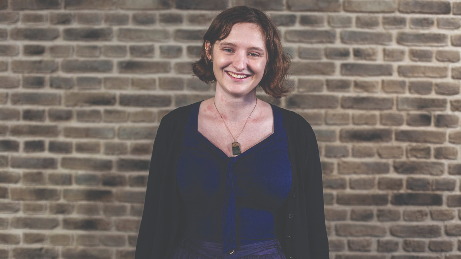 Kaitlin stands in front of a brick wall smiling into the camera.
