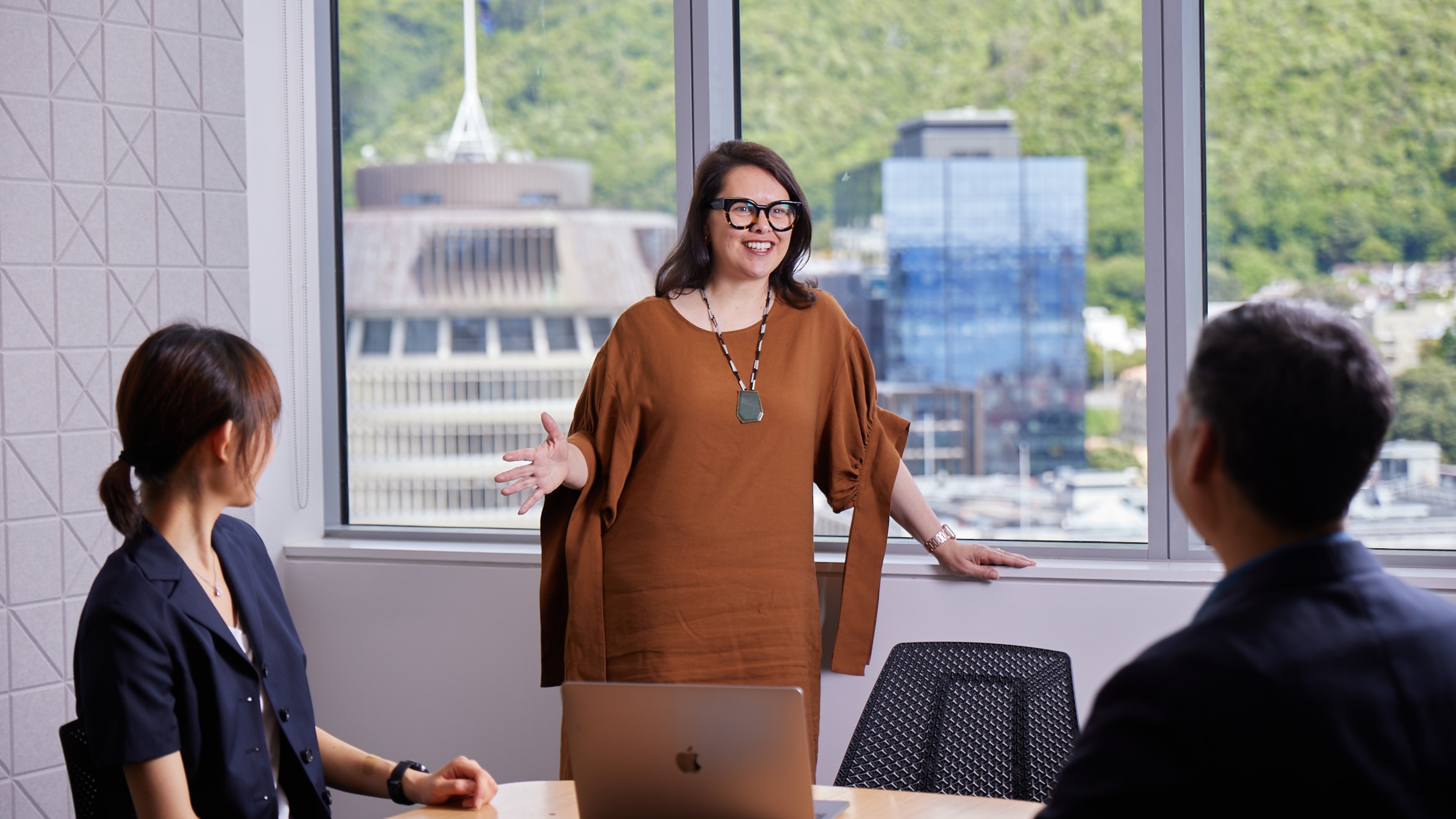 A person speaks with colleagues in an office room with the Beehive in the background.