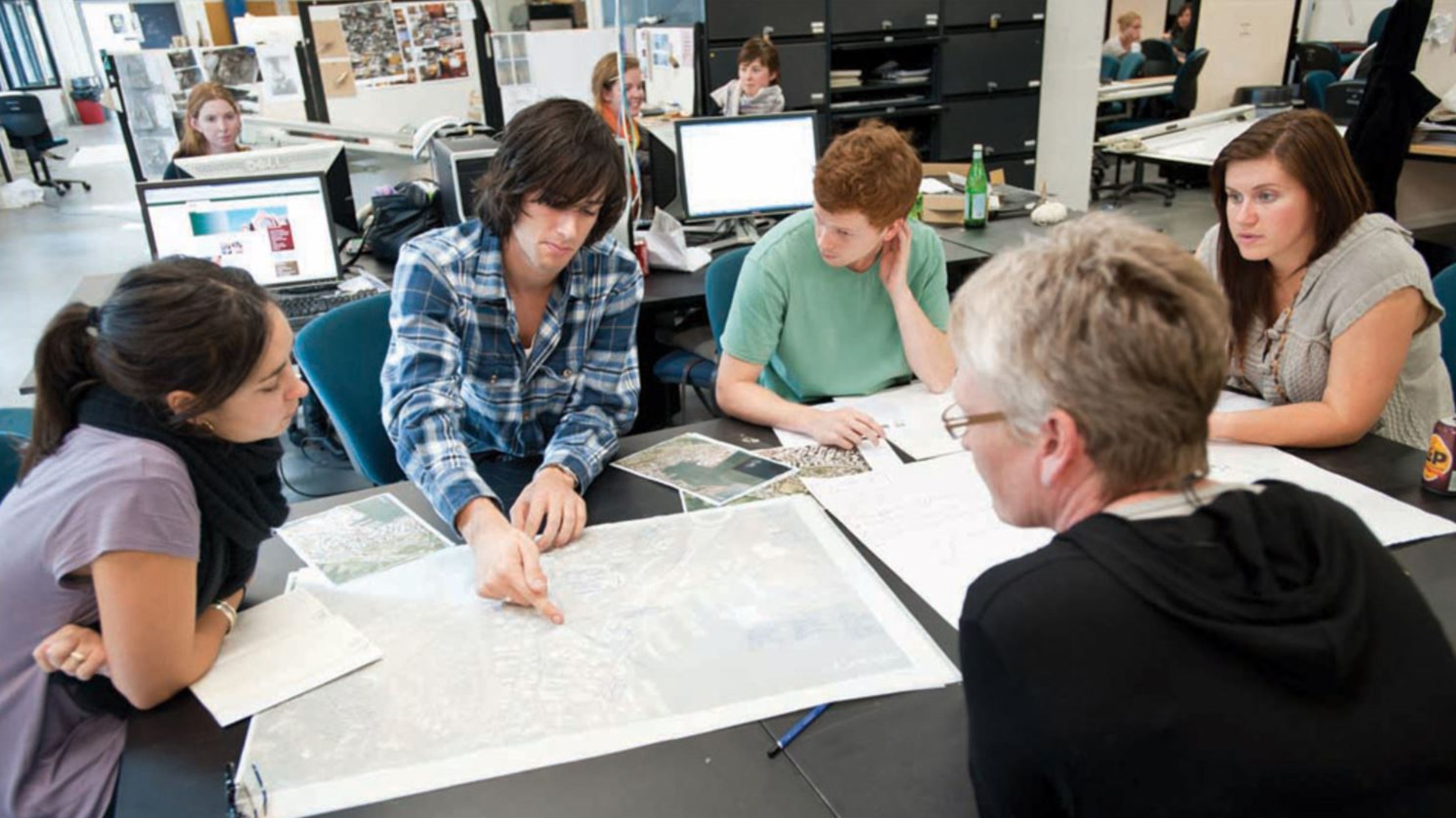 Four students and a tutor sit around a table looking at a map
