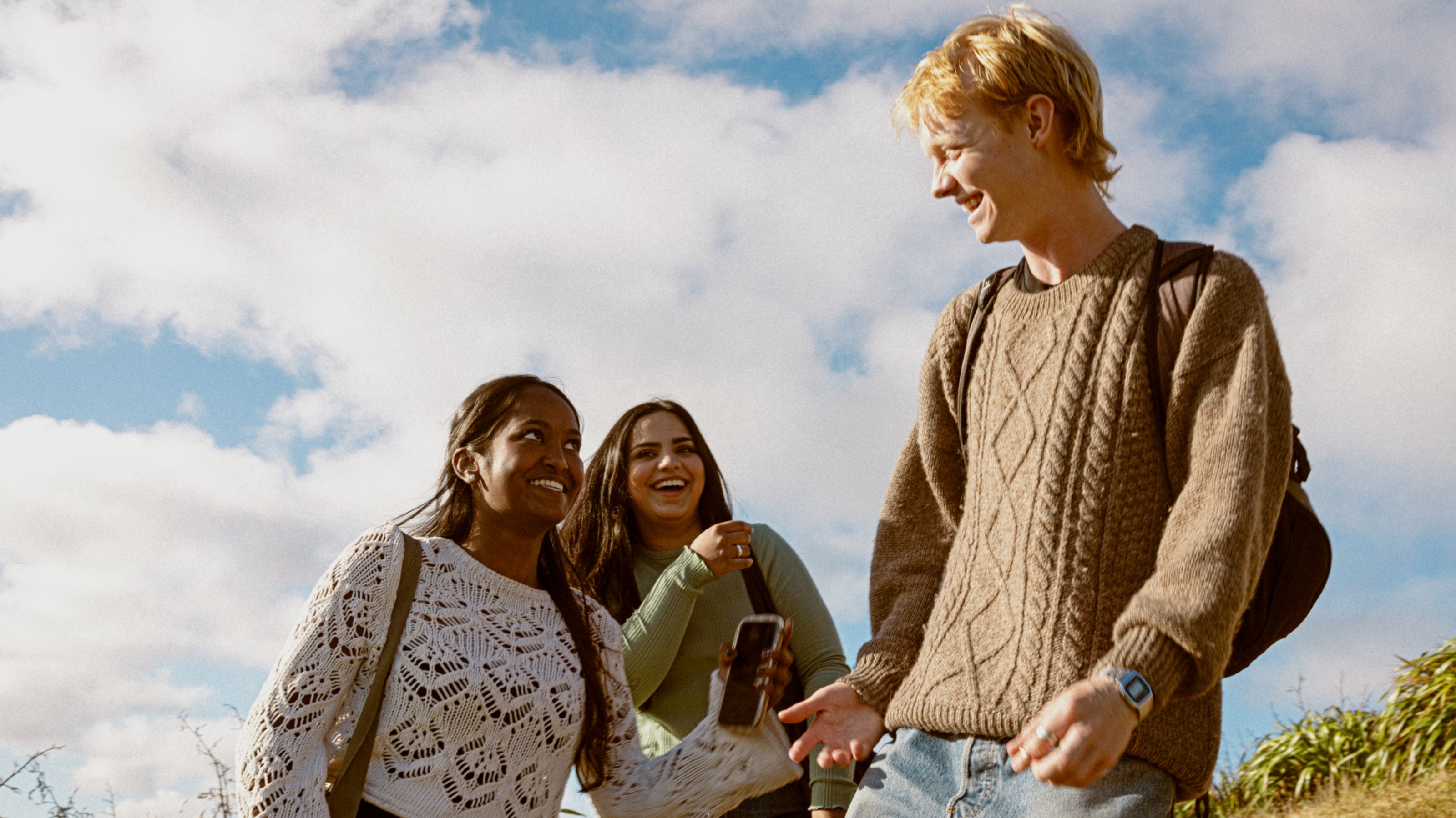 Three students walking up Mt Vic, with blue sky and clouds in the background