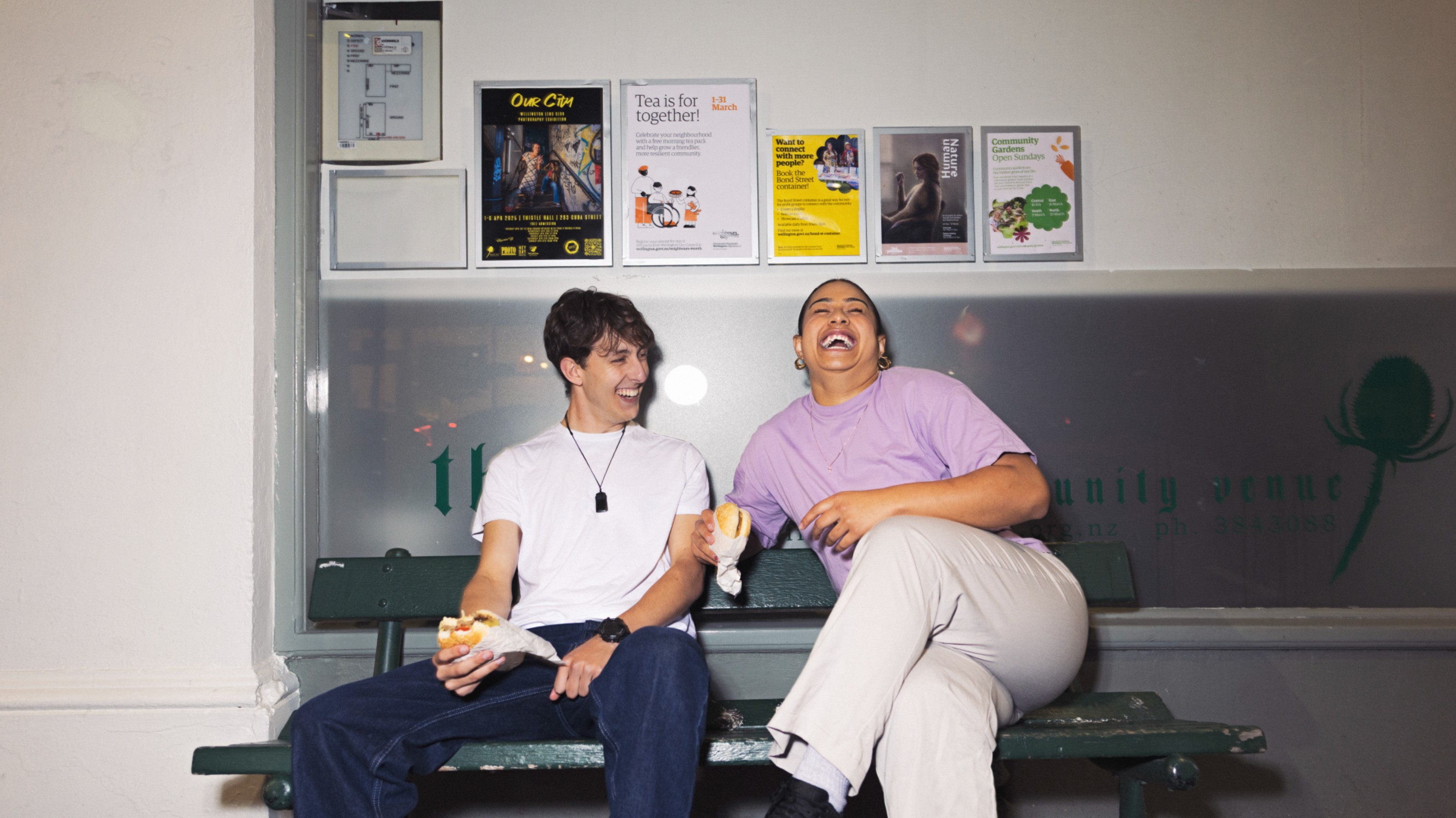 Two students sitting on a bench laughing, eating burgers