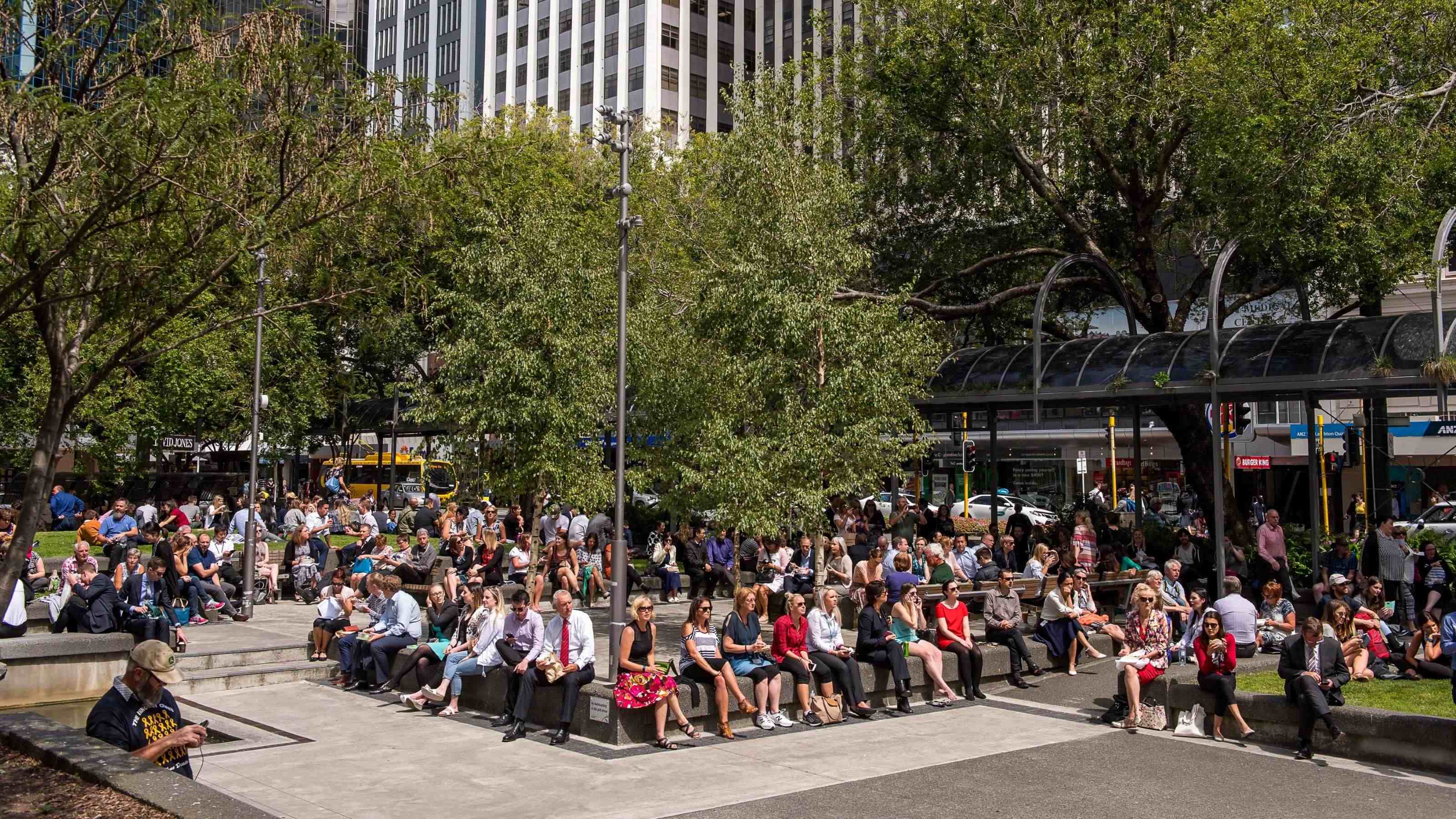 Crowd of people sitting in a central city park at lunchtime.