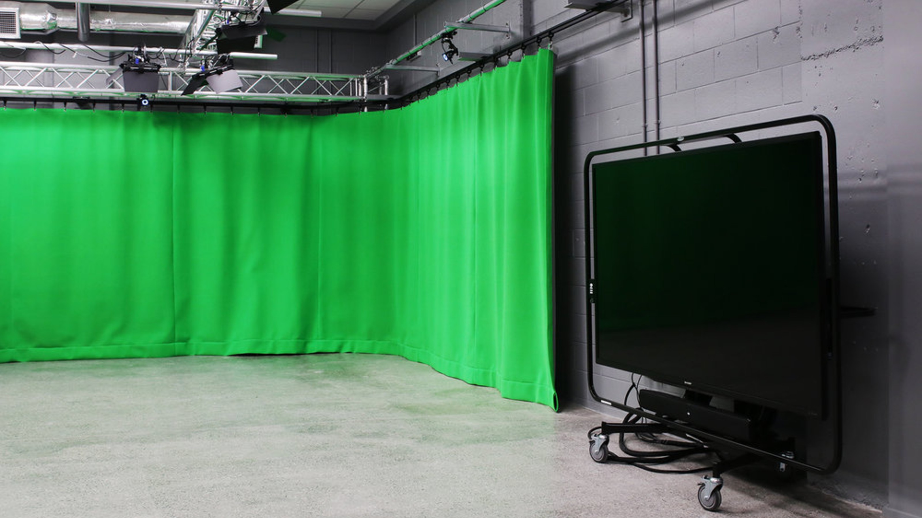 Studio with grey walls, green curtain, large screens.