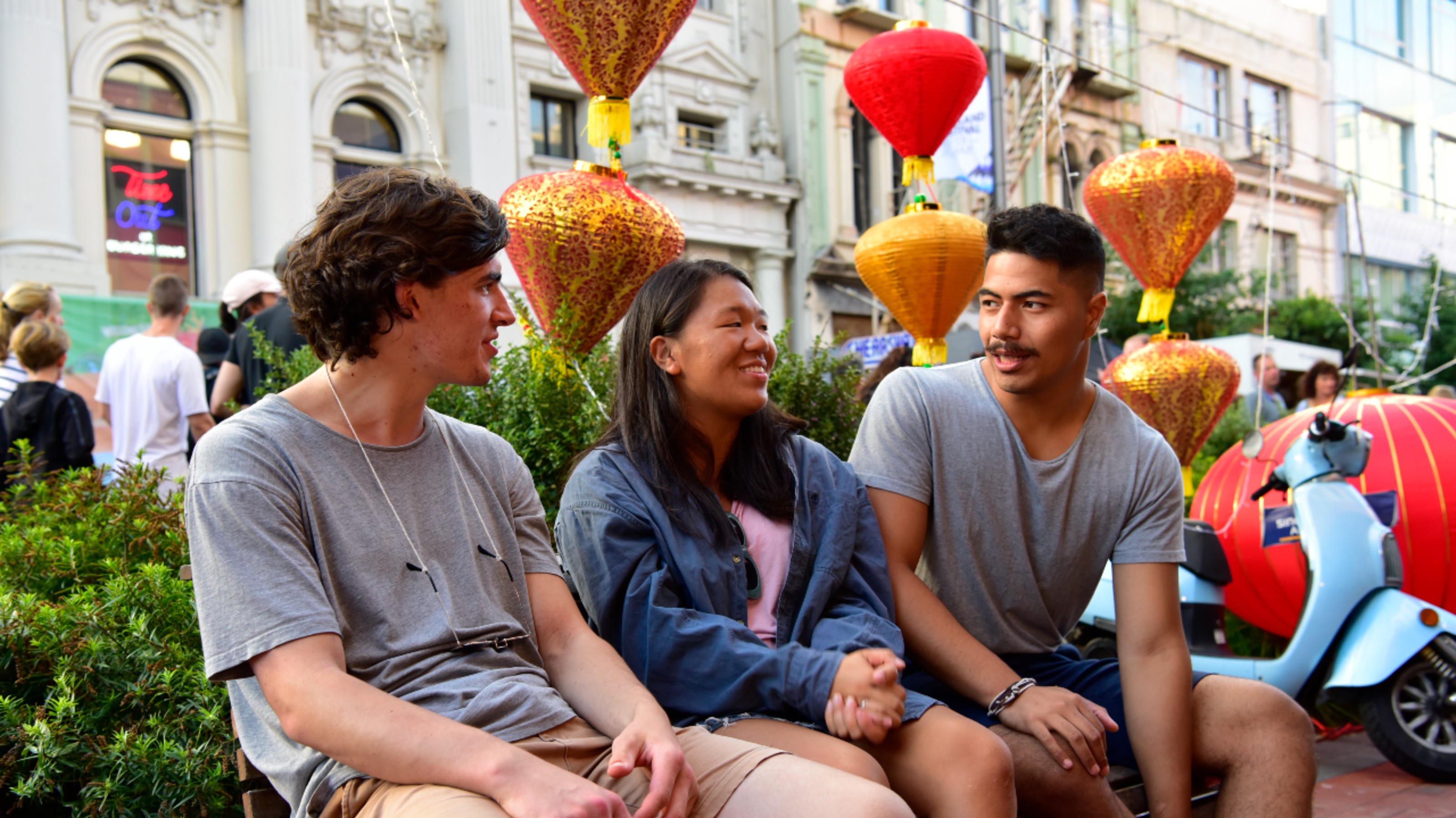 Three students speaking at a lantern festival, one student is feminine and two are masculine.