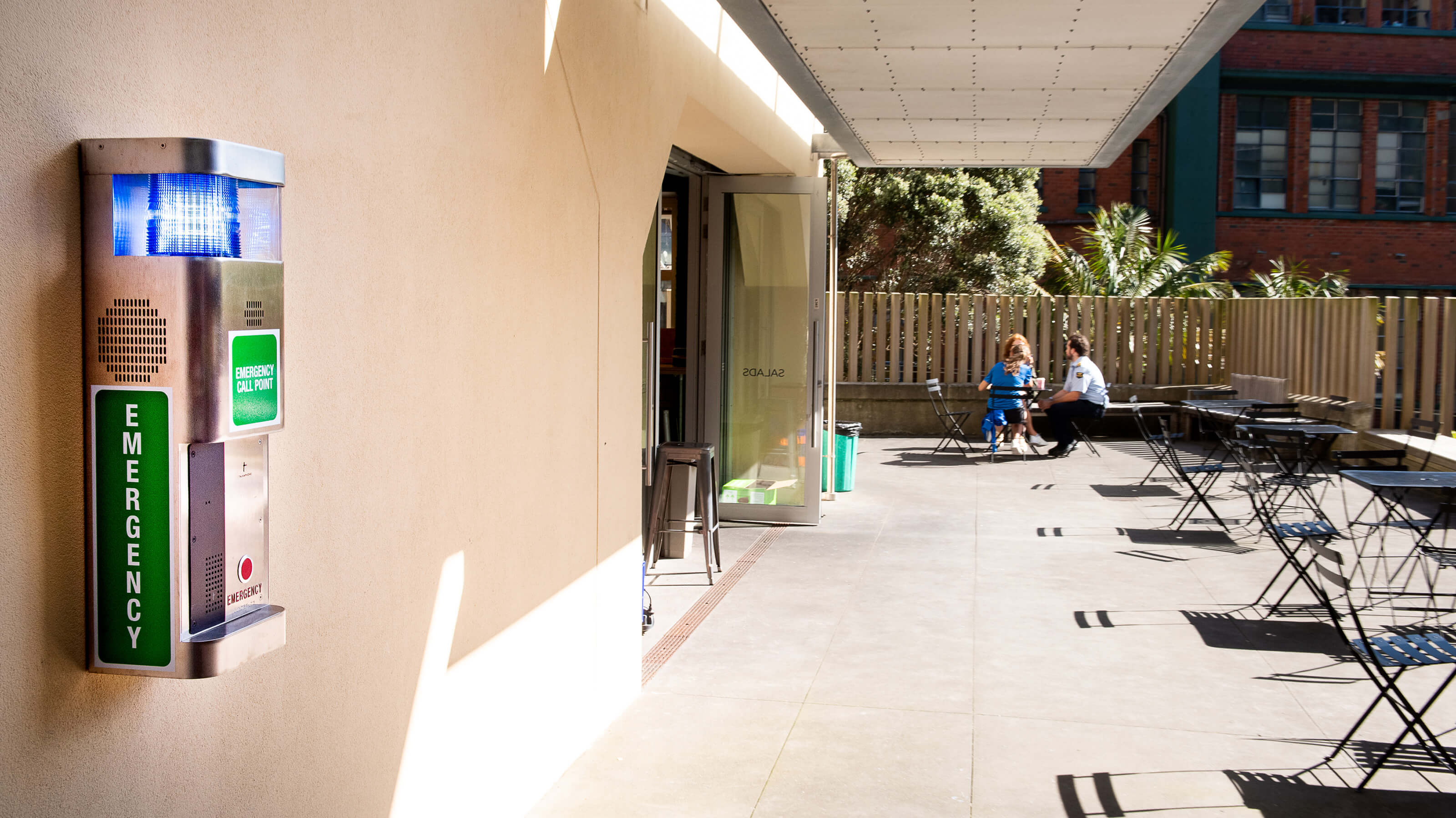 Emergency call point near courtyard full of cafe tables.