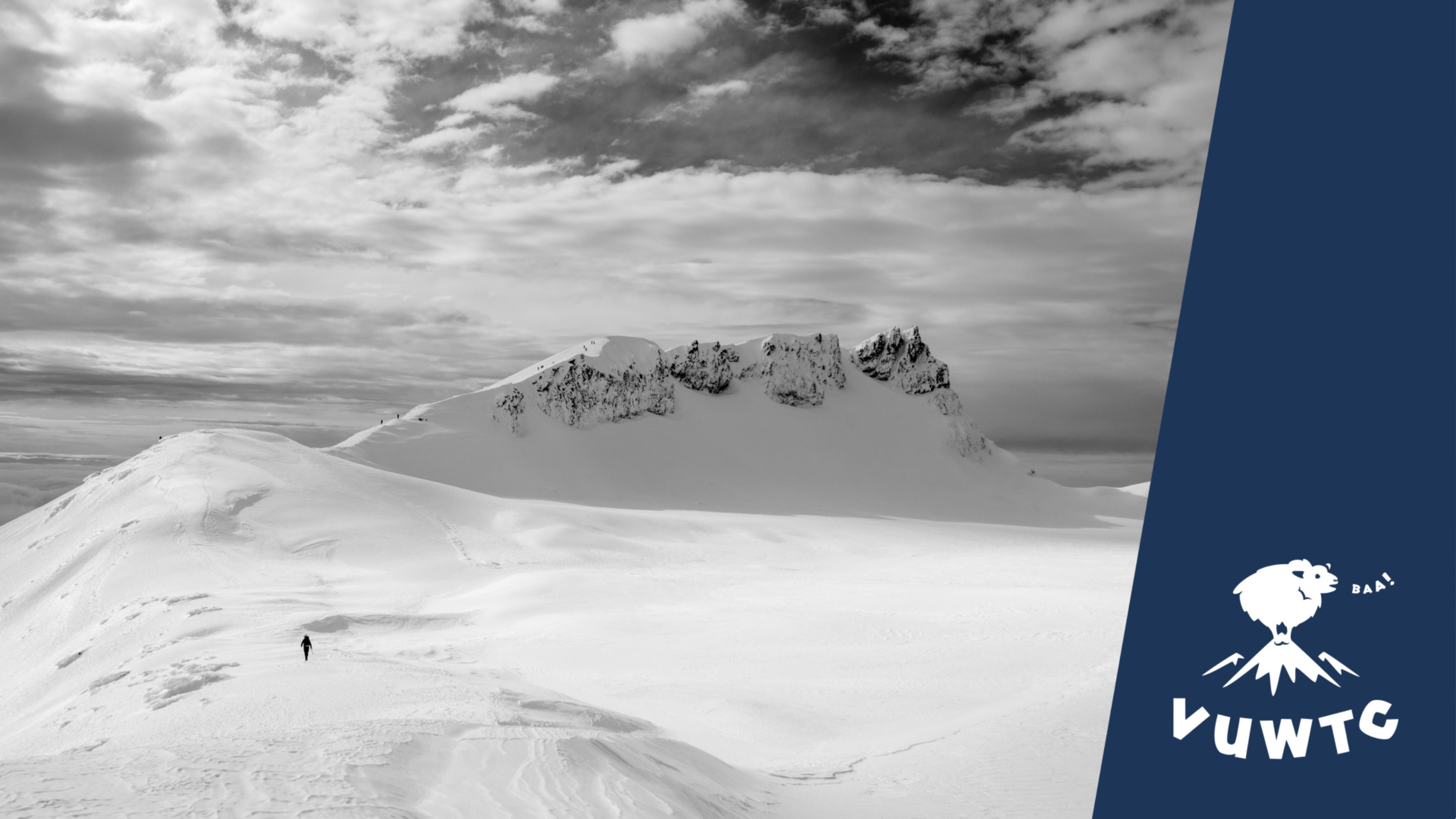 Black and white landscape of snowy mountains, with small silhouette of a tramper.