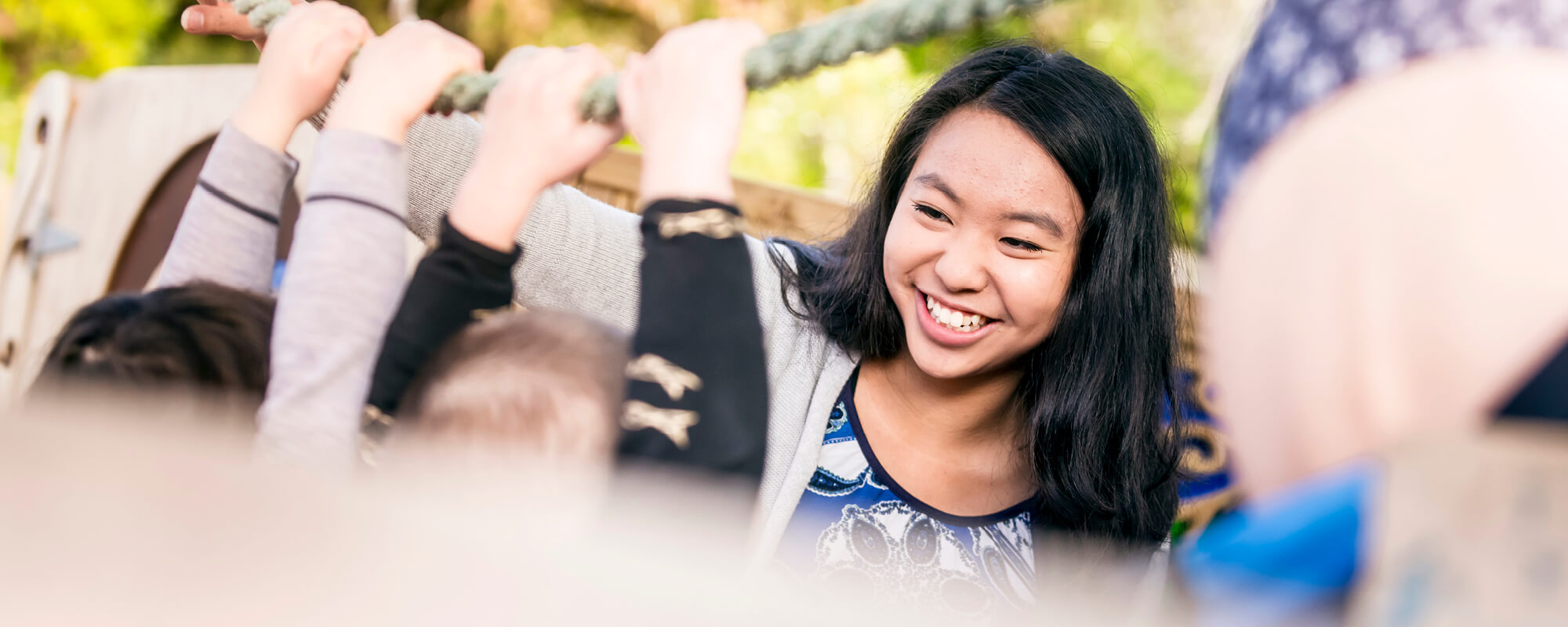 A smiling early childhood teacher is playing with some children on a rope swing.