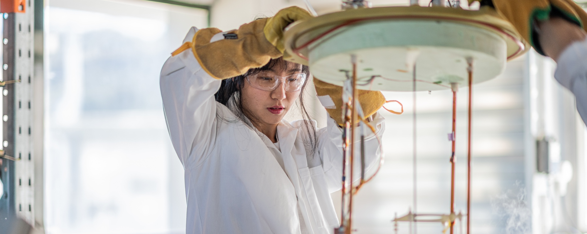 Young Asian woman researcher lowering scientific equipment into liquid nitrogen.