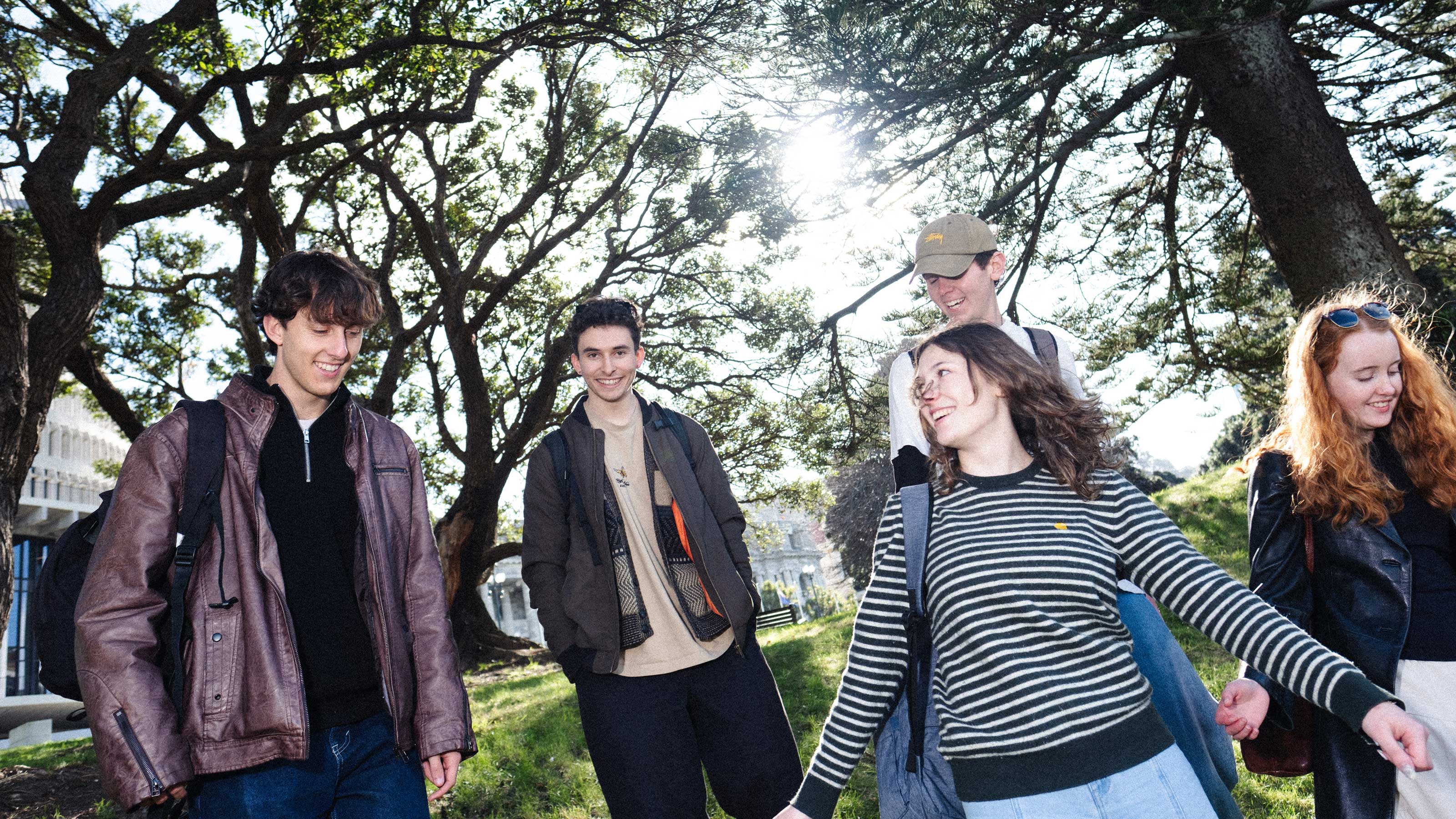 Five students walking beneath trees outside the Beehive