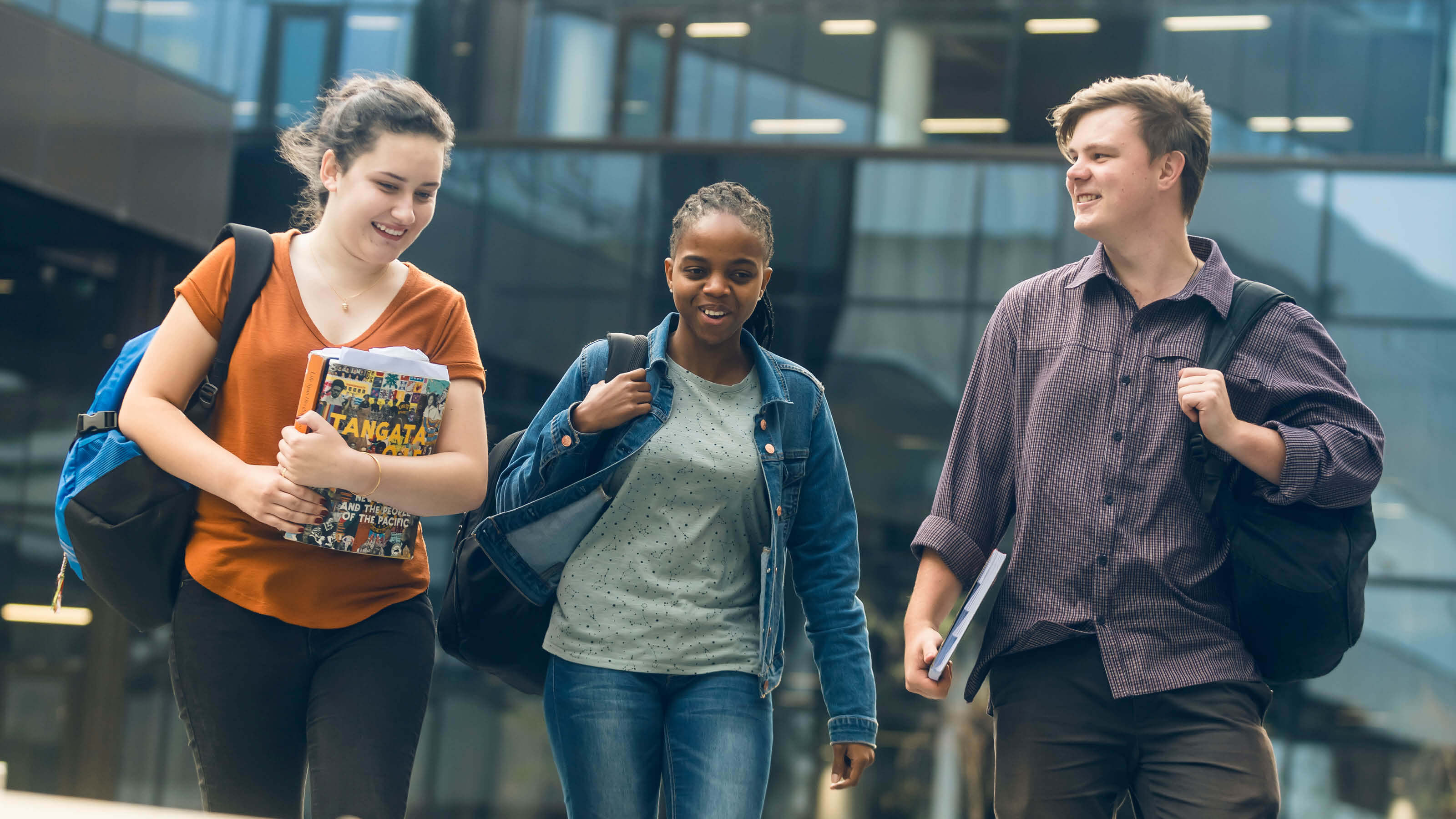 Three students walking across the courtyard in front of Te Toki a Rata building on Kelburn campus.