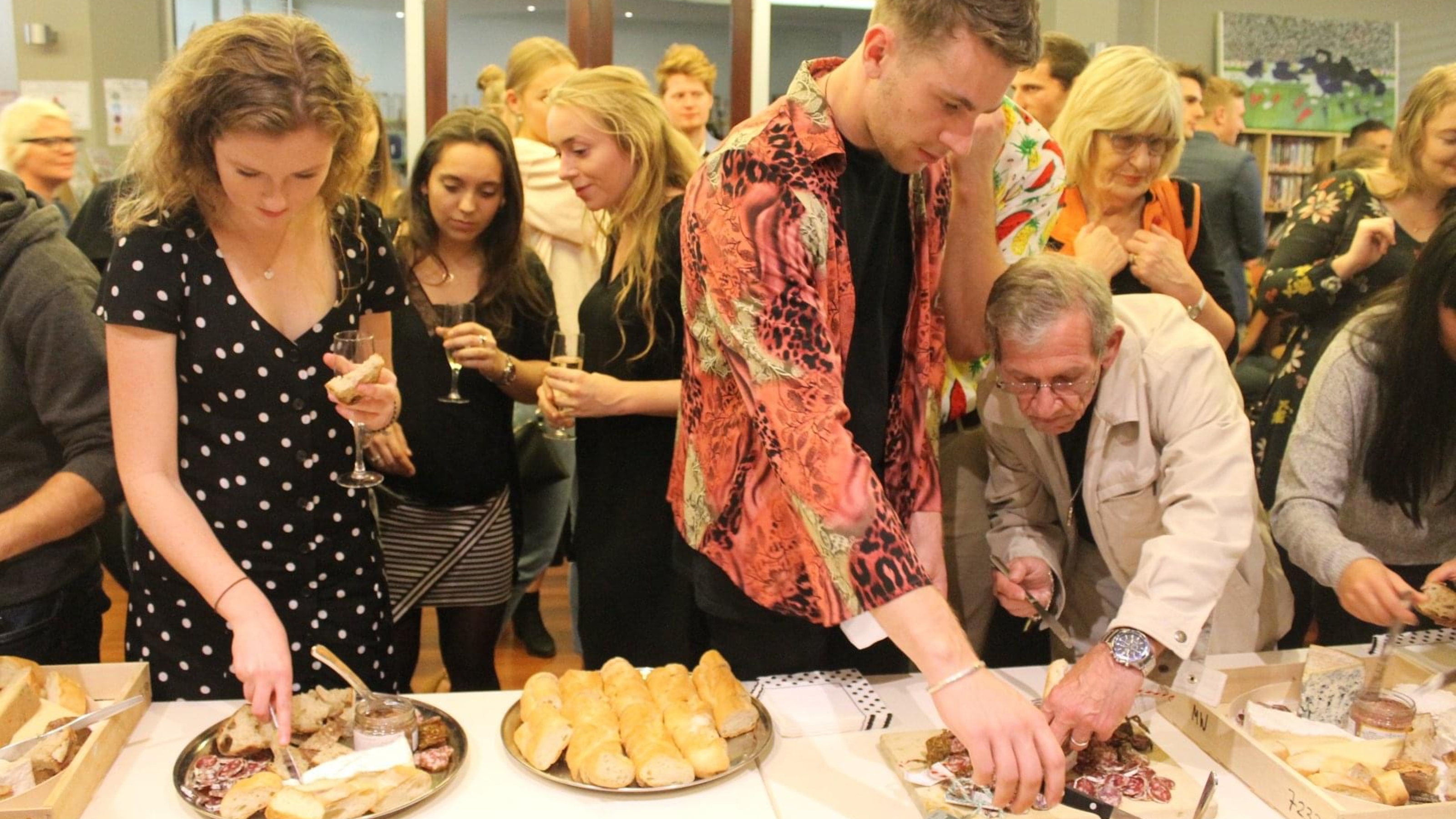 Society members helping themselves at buffet with saucisson, baguette, and cheese.